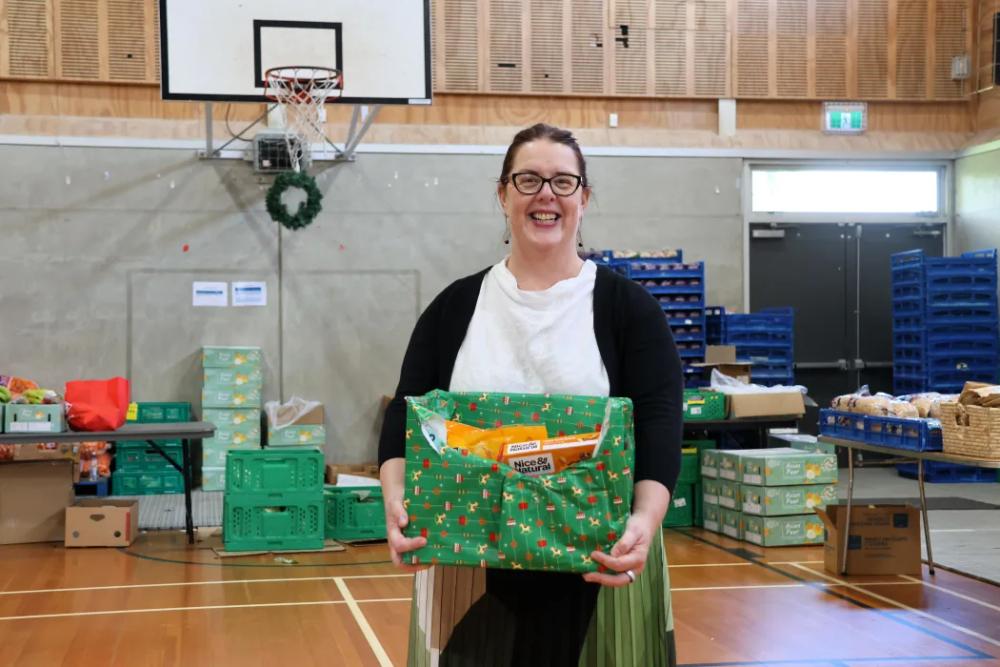a woman smiling at the camera holding a box of donated food