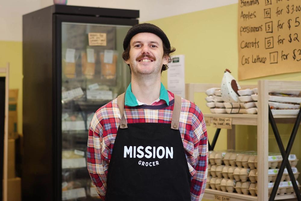 a man wearing an apron is standing in a grocery store .