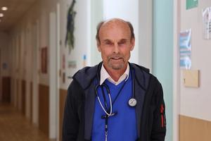 a man with a stethoscope around his neck is standing in a hospital hallway .