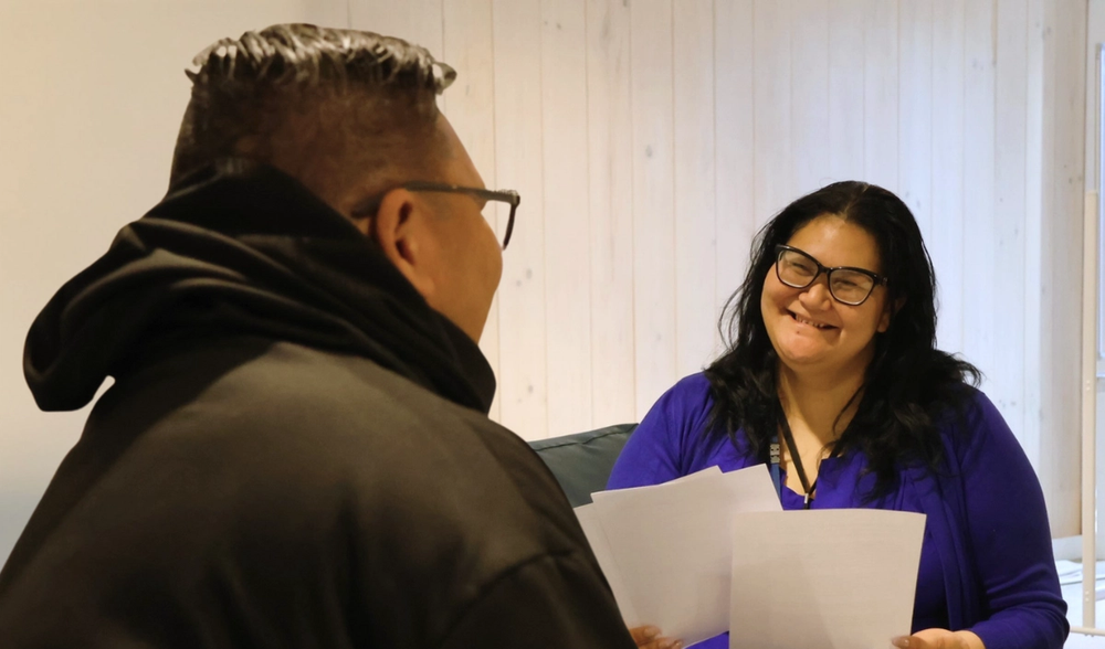 a woman wearing glasses holds a piece of paper in front of a man