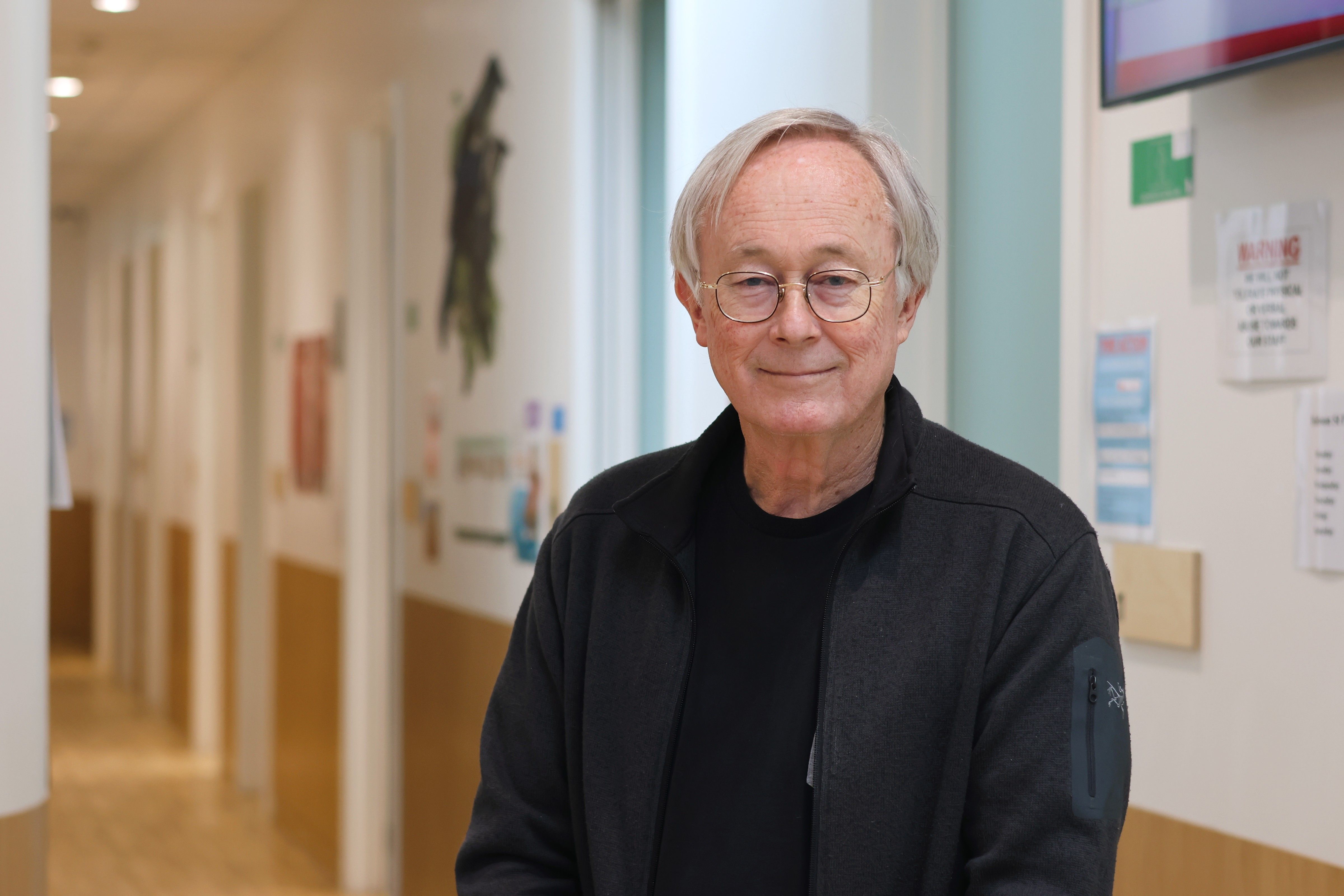 a woman wearing glasses and a lanyard is standing in a hallway and smiling .