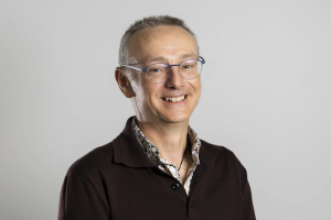 a man wearing glasses and a maroon shirt smiles for the camera