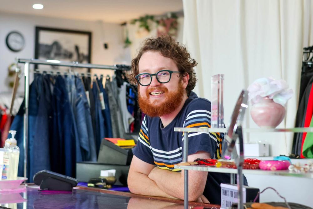 a man with a beard and glasses is sitting at a counter in a clothing store .