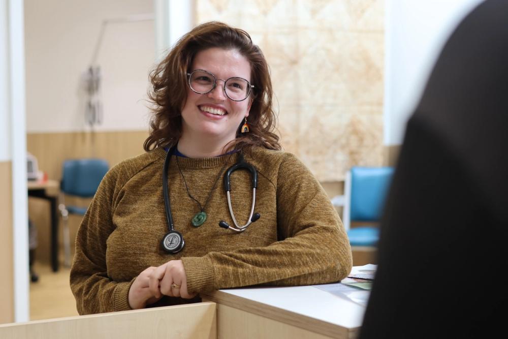 a woman with a stethoscope around her neck is smiling at a patient .