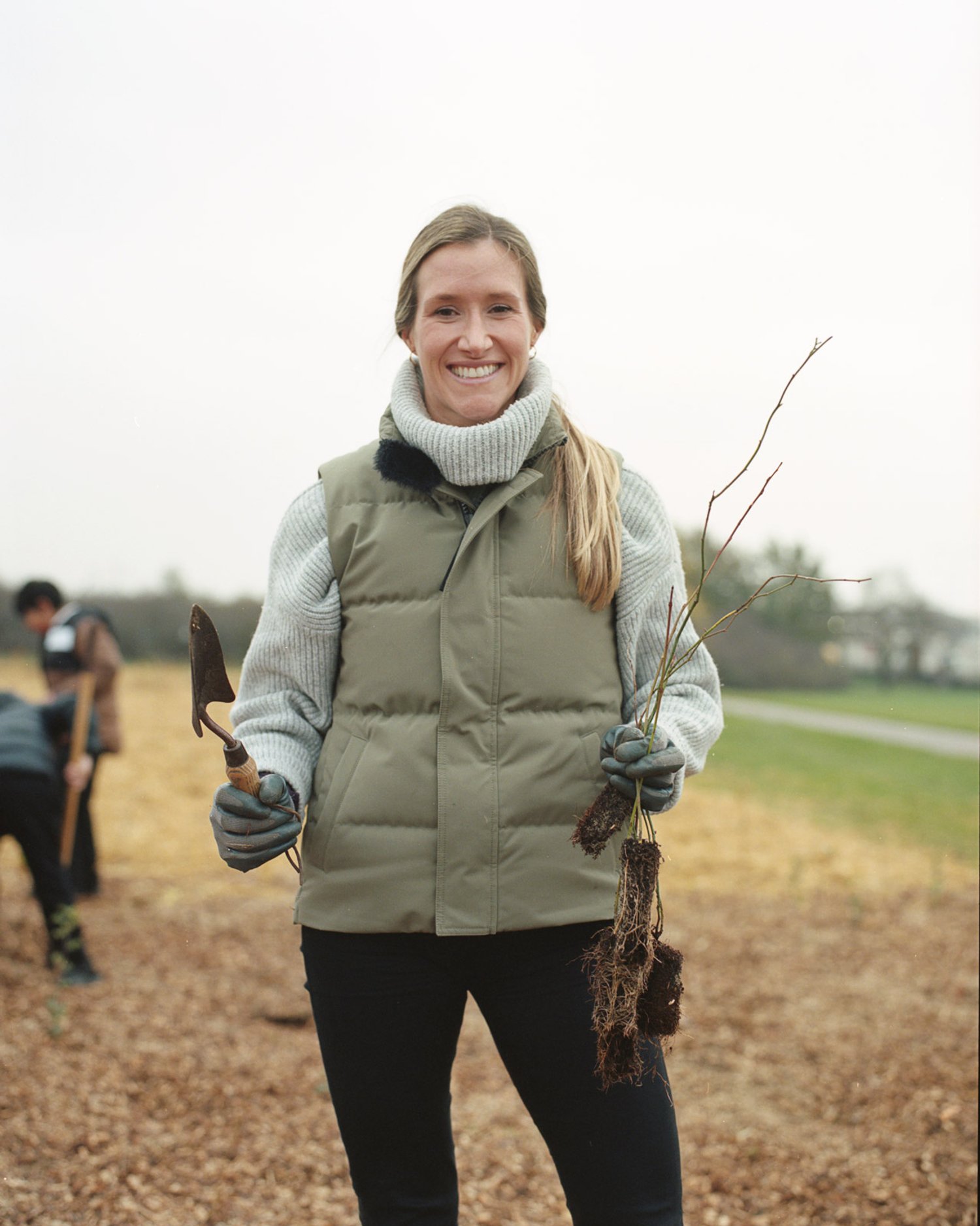 a woman stands holding a tree sapling