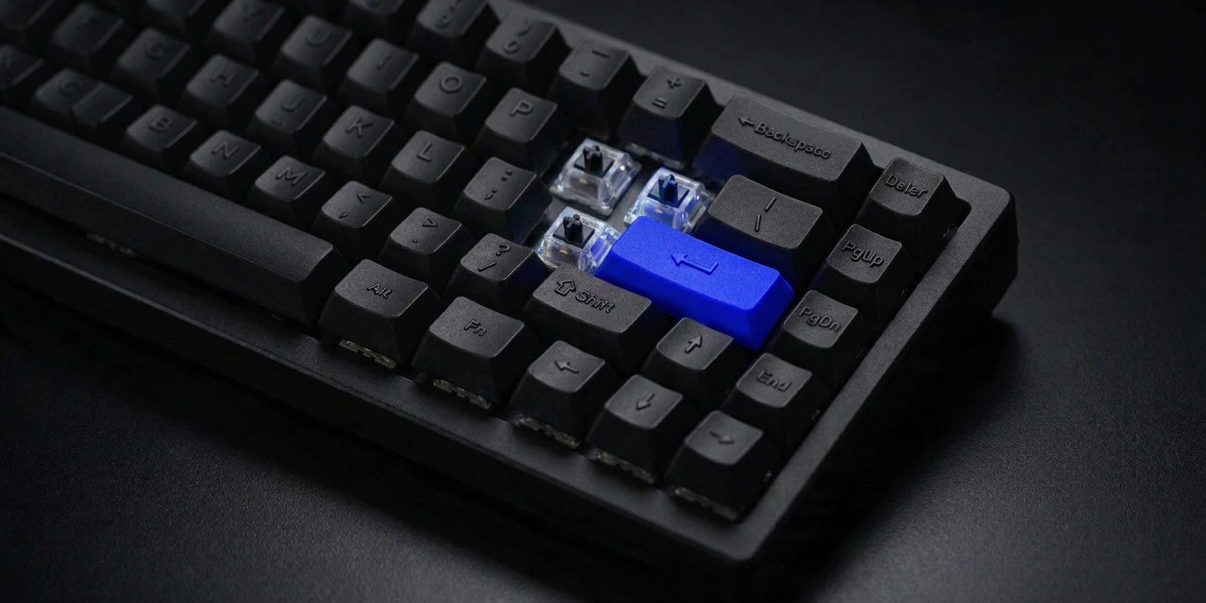 Close-up of a black mechanical keyboard with an electric blue Enter key and the curly brace keys removed