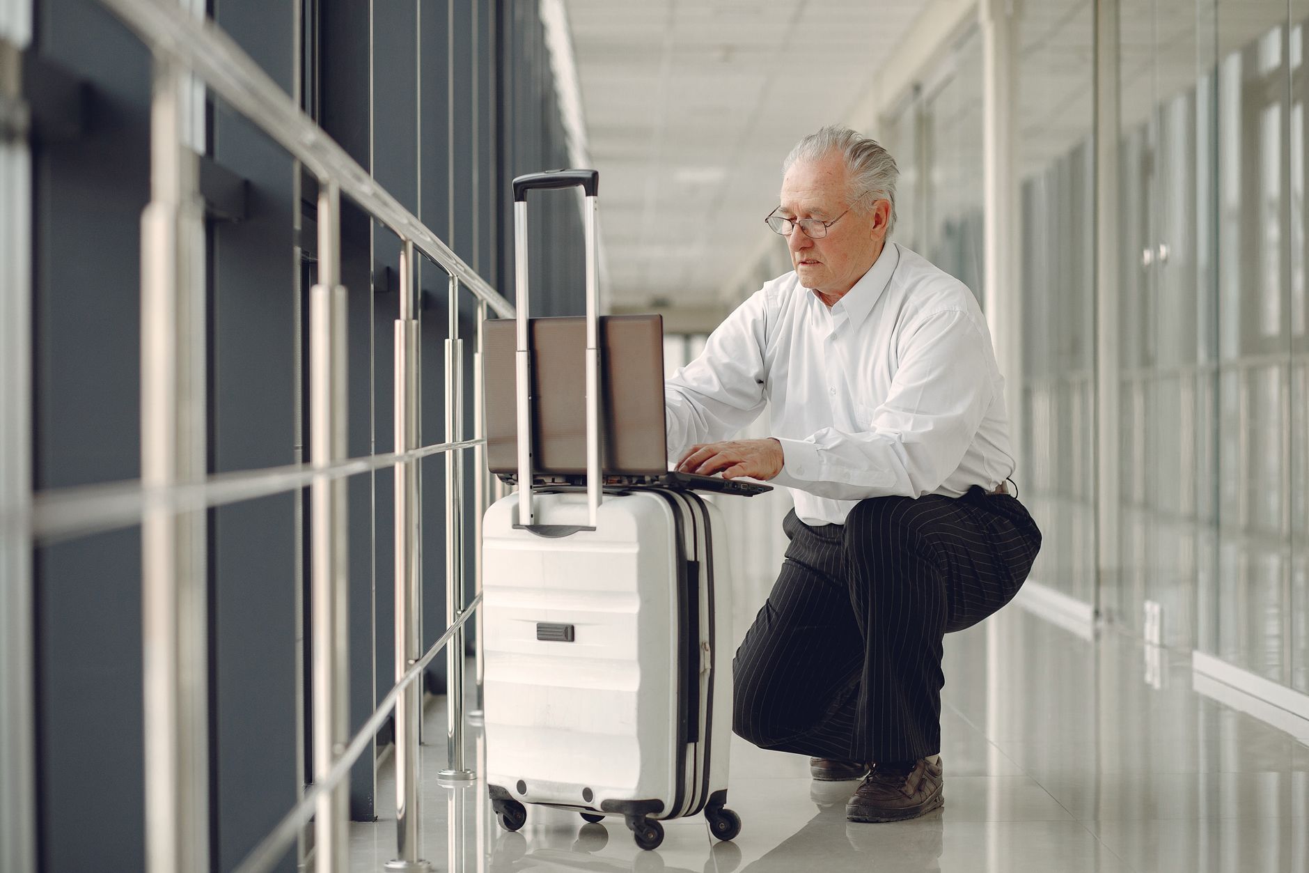 A business traveller working on a laptop balanced on luggage in an airport