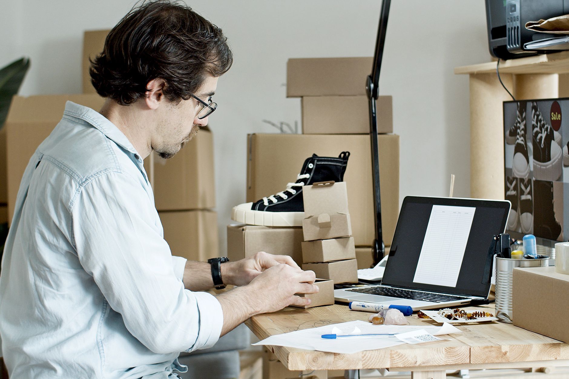 A small business owner at a laptop surrounded by packed order boxes — the moment a brand's order-confirmation and invoice emails, sent through a newly added third-party platform, either authenticate cleanly or silently fail to reach the customer