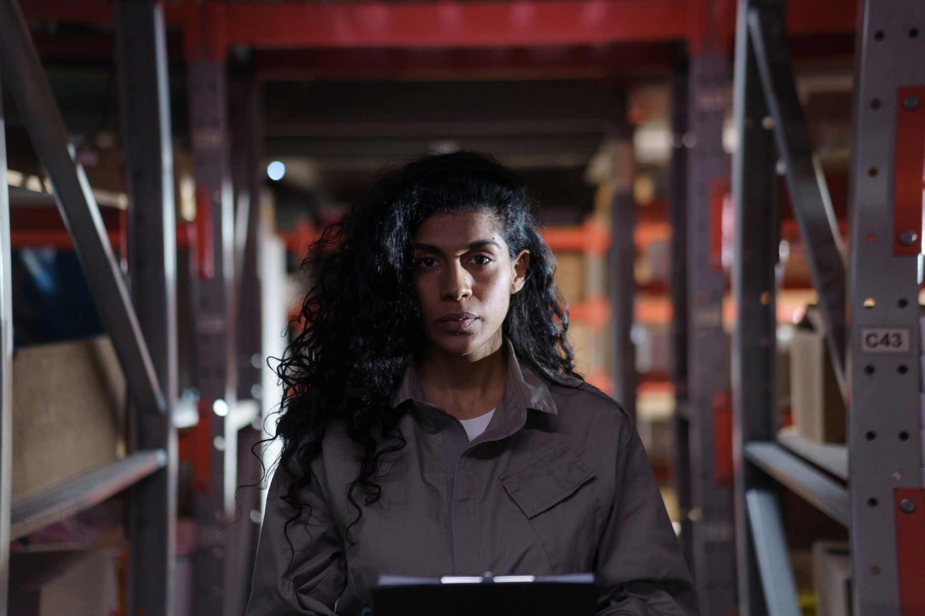 One person alone in a warehouse aisle with a clipboard — the single embedded engineer a Singapore warehouse depends on, and who is not there on the days they take leave, fall ill or hand in their notice