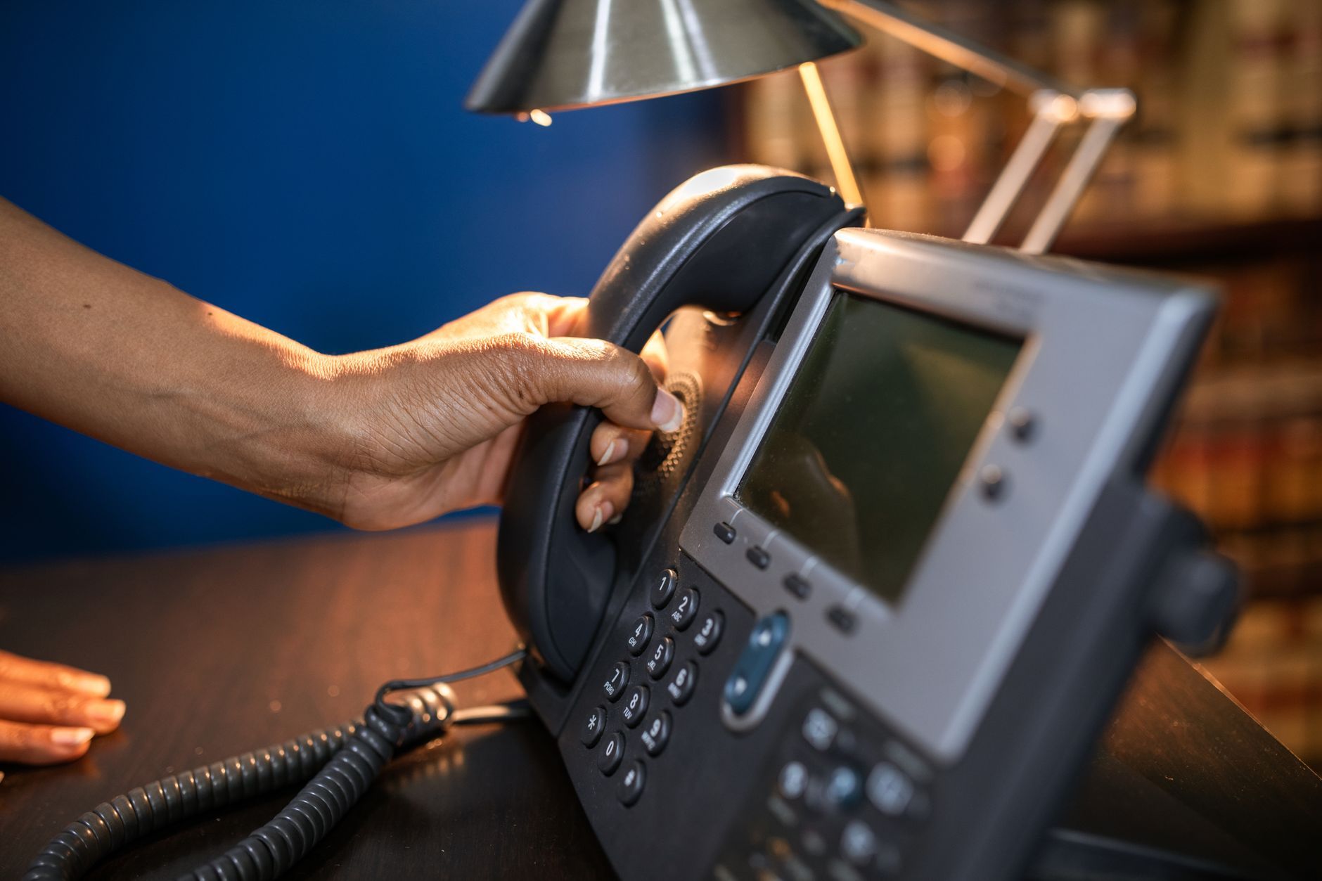 A hand lifting the handset of an office telephone on a desk, representing a call arriving on a company number rather than an individual's mobile