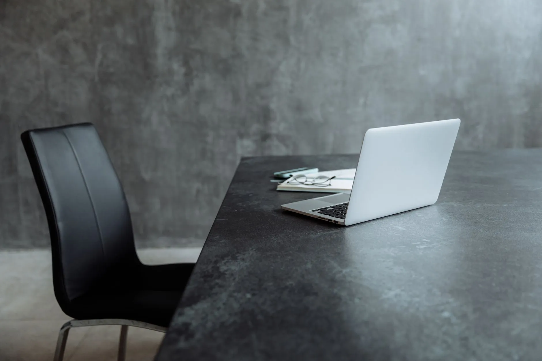A minimal desk with a single laptop and a leather office chair — day one for a newly licensed Hong Kong asset manager in a serviced office: one tenant, two laptops, and everything else still to build