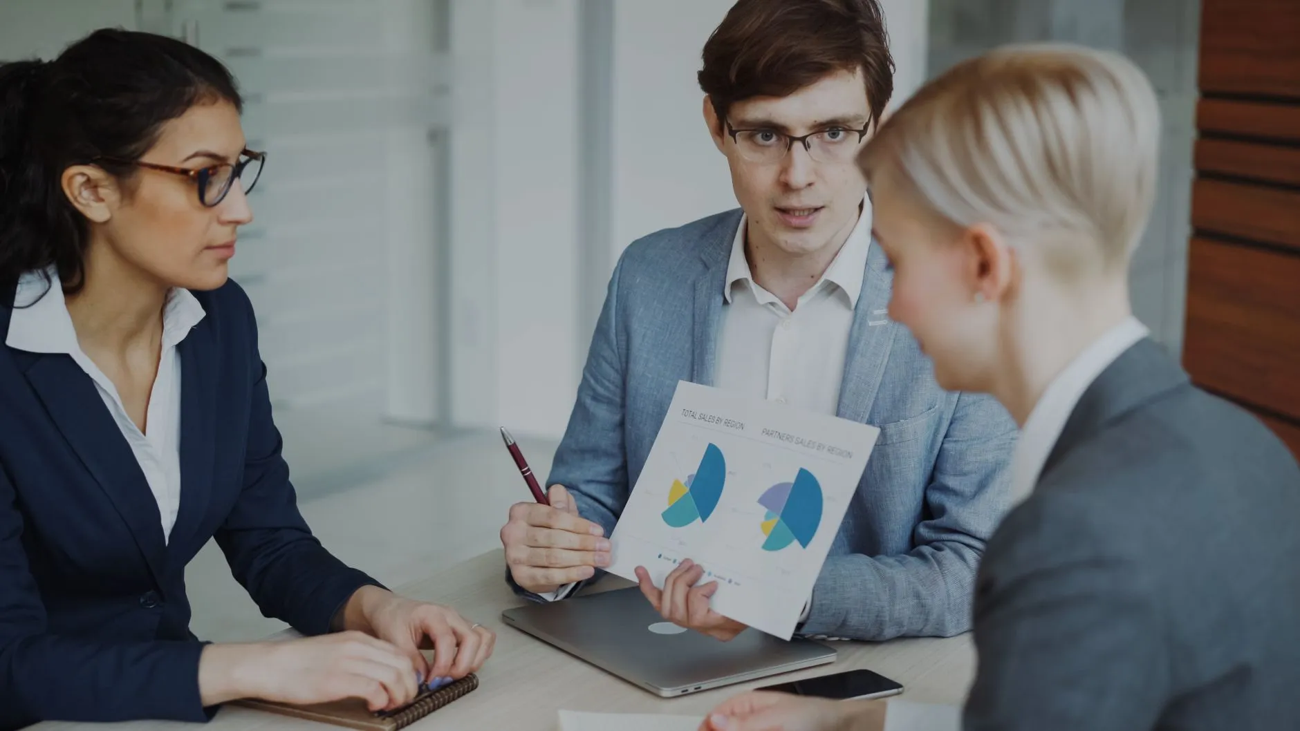 A team of professionals discussing sales strategy around charts and a laptop in a modern office