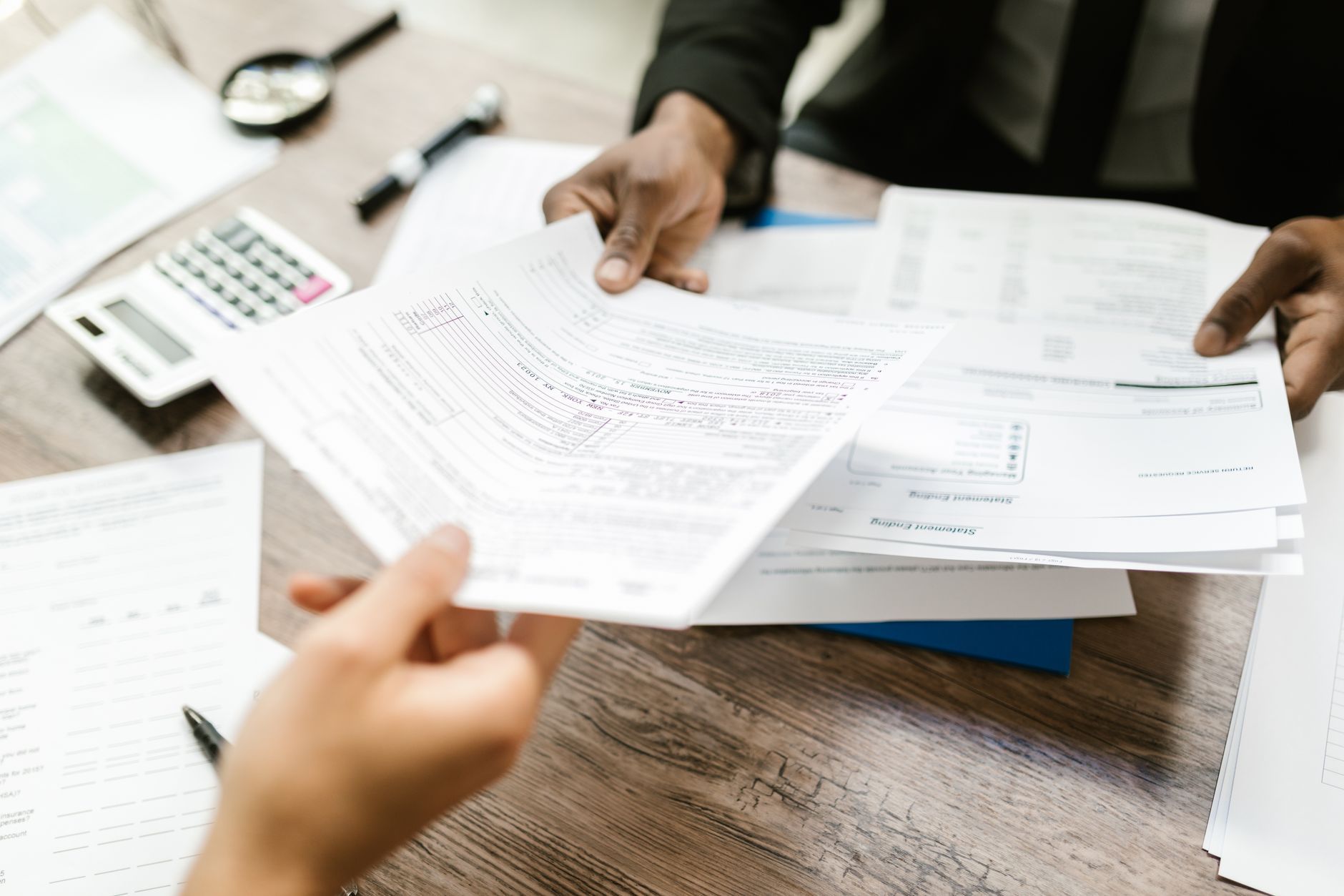 Two professionals across a desk, one handing over a document to the other — the moment a buyer asks a provider to produce a record