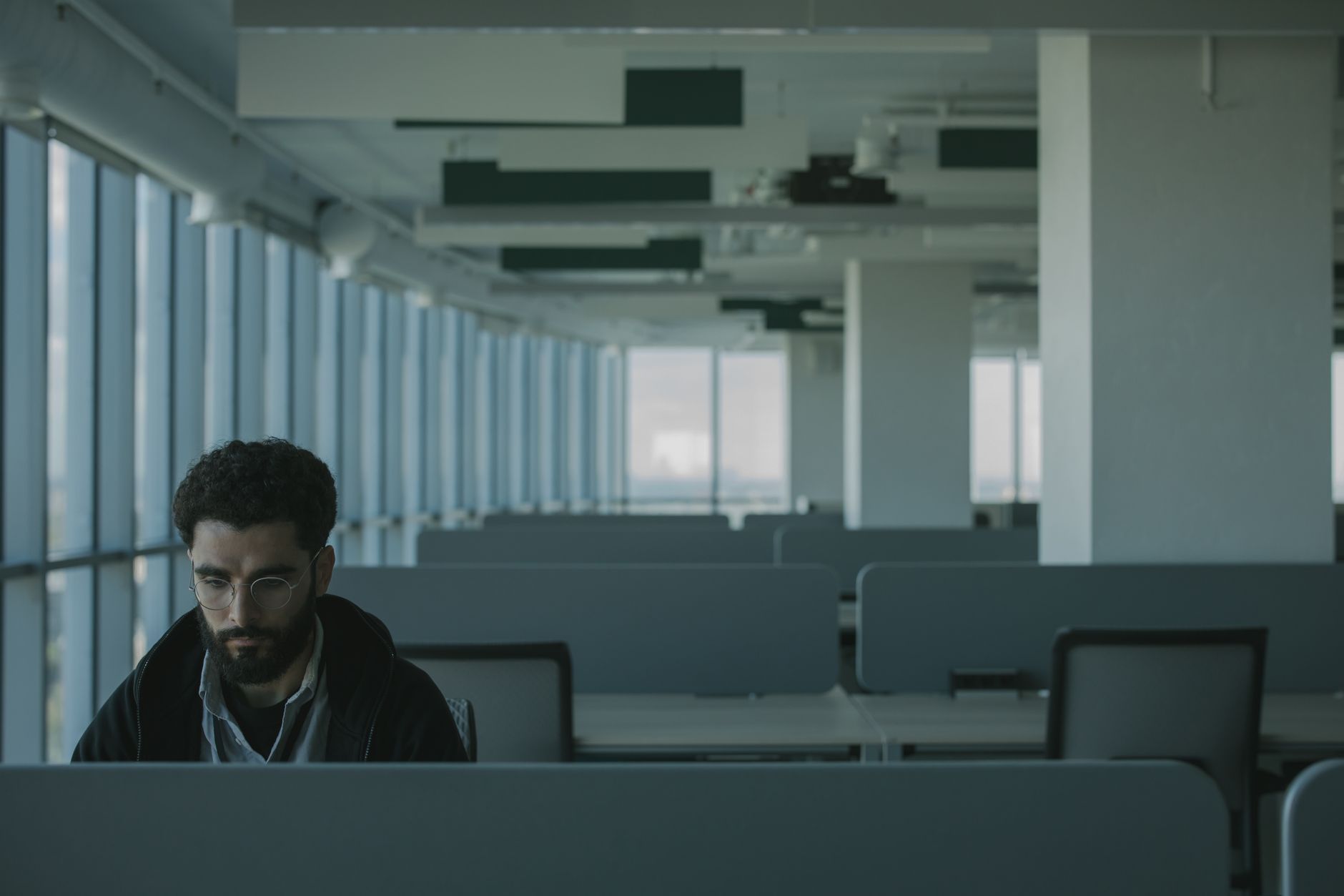One person working alone in an otherwise empty office — the sole IT manager whose undocumented knowledge of the whole estate is about to walk out of the building with them