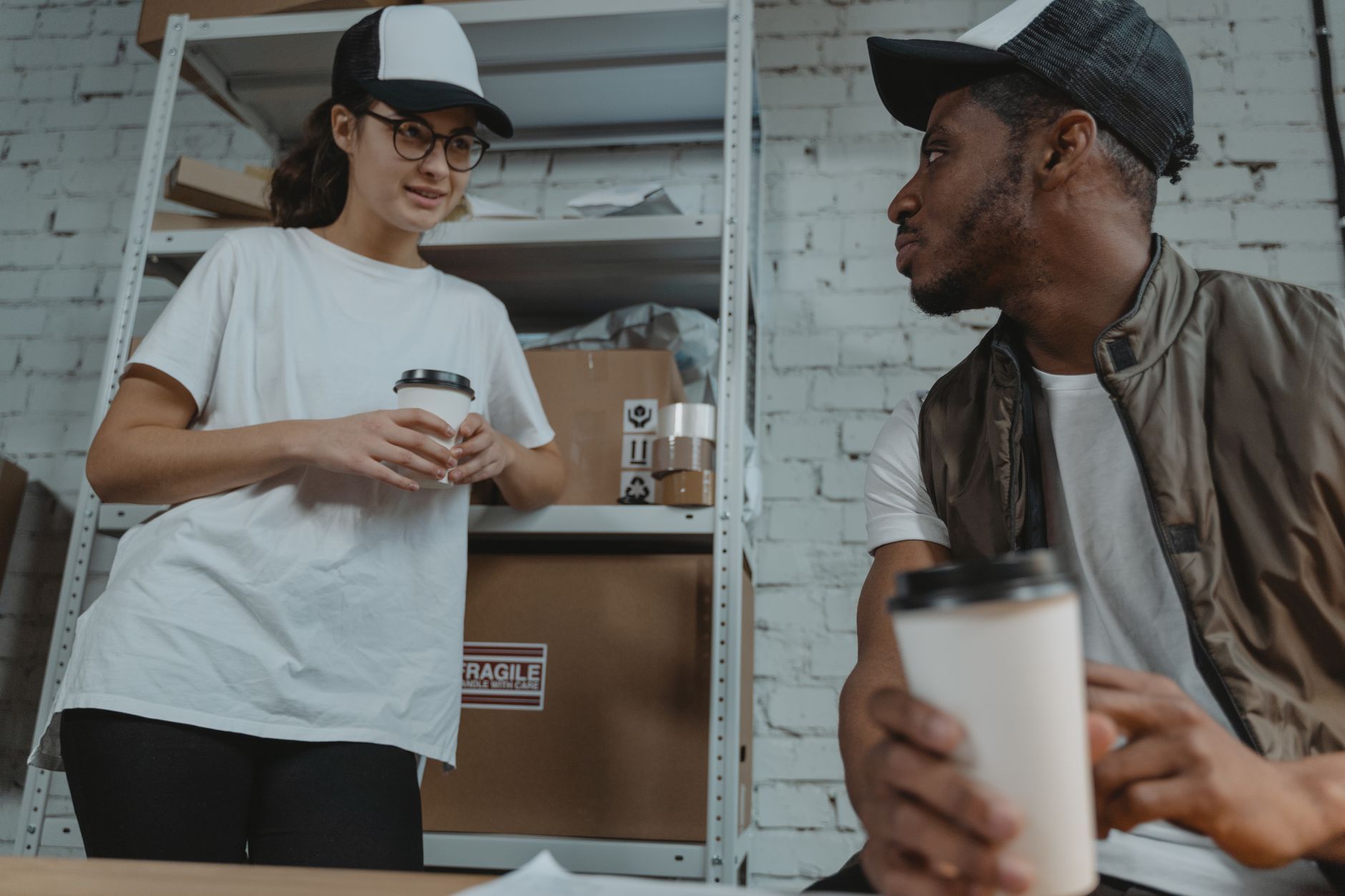 Two colleagues talking on a warehouse floor — the user-facing conversation that happens in the local language, while the ticket, the asset record and the vendor escalation it produces will all be written in another