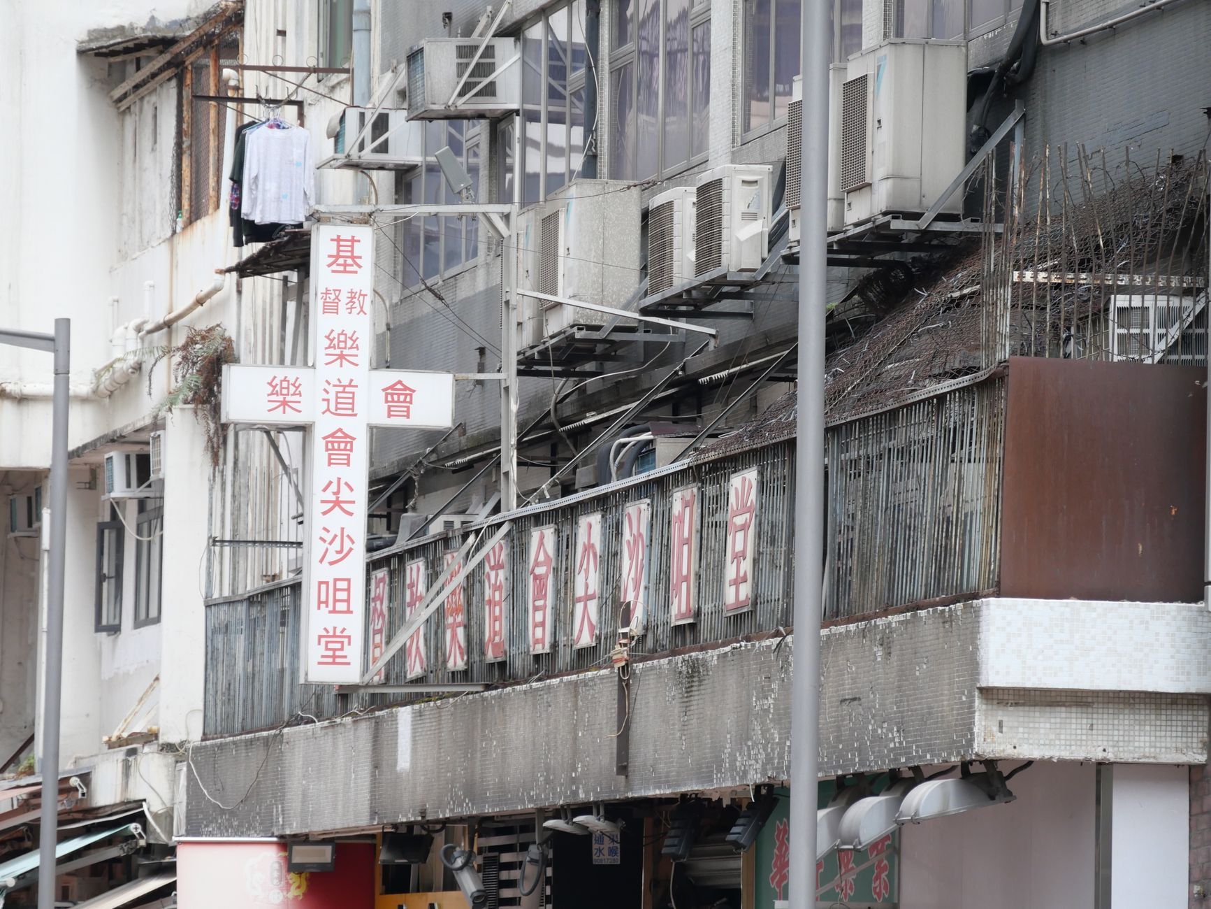 Street-level view of an older Hong Kong building facade covered in air-conditioning units and Chinese signage, typical of the converted industrial blocks in Kowloon East