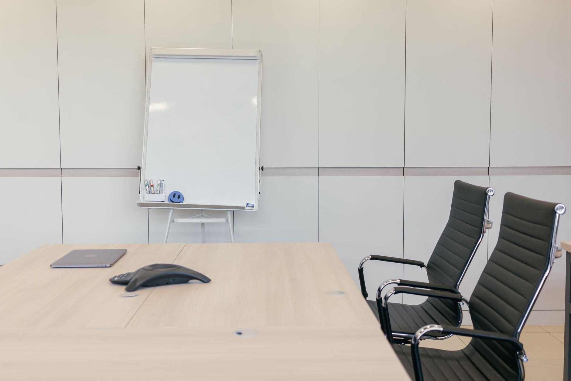 An empty office meeting room with a table, chairs and a whiteboard, the kind of room where a shared Wi-Fi password ends up written in the corner for visitors