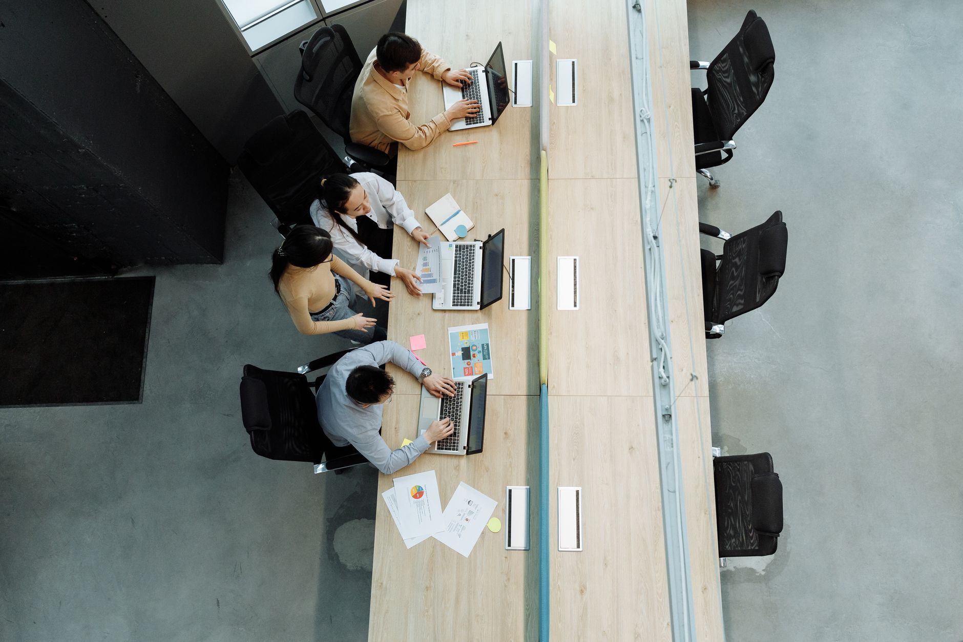 High-angle view of colleagues on laptops at shared desks in a bright open-plan office, the dense floor an active wireless survey tests under load.