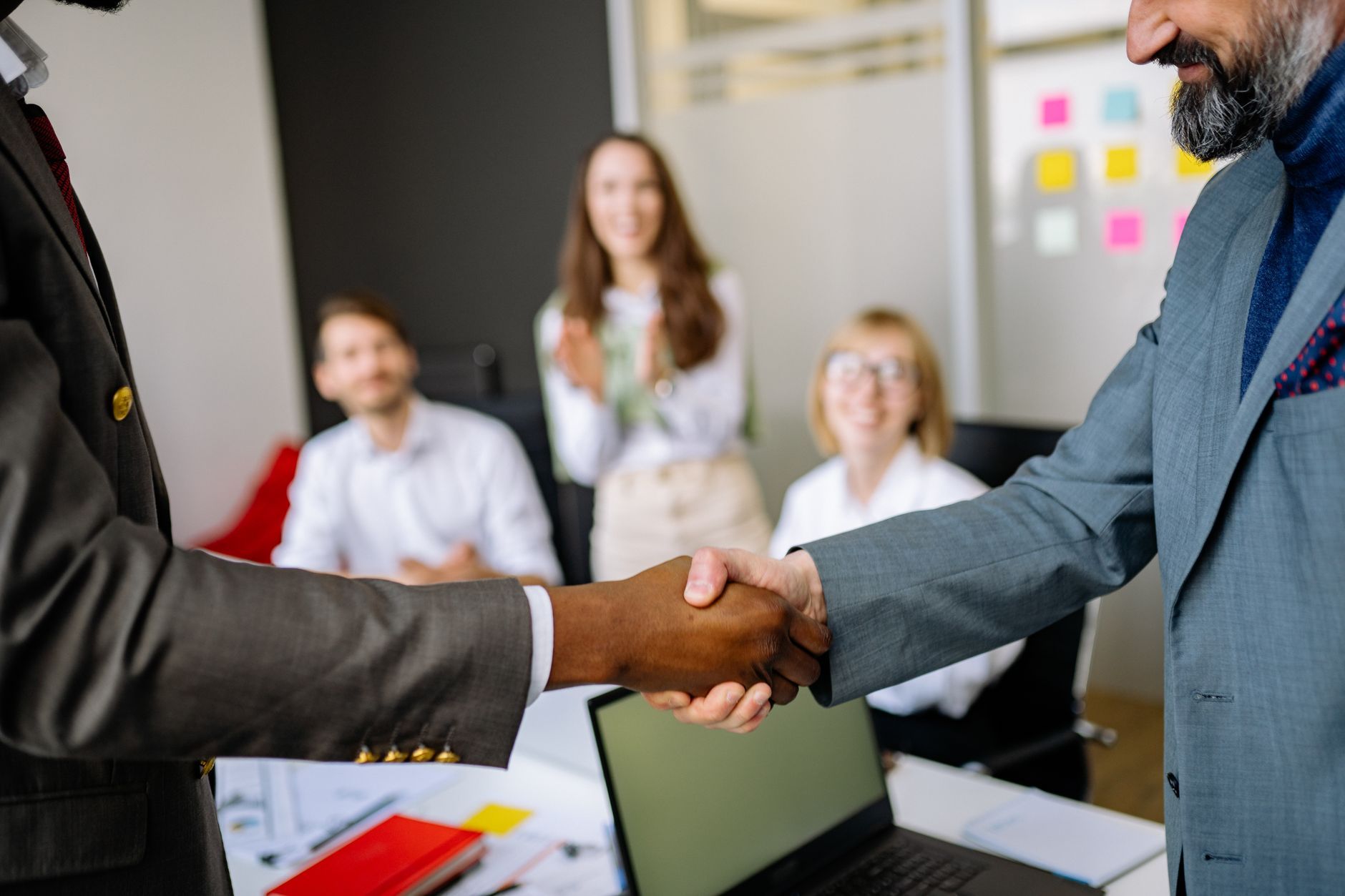 A handshake between two colleagues in a professional office, representing an on-site IT engineer being rebadged onto a new employer's payroll without leaving the site