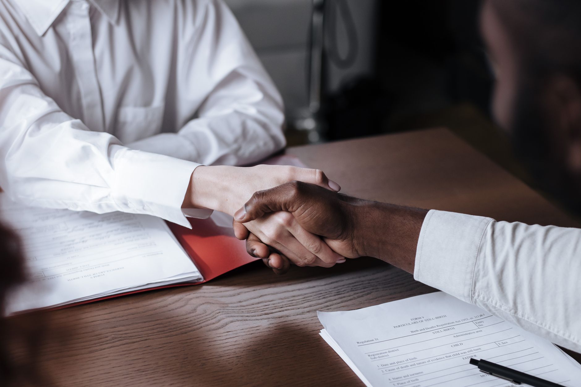Two people shaking hands across a desk covered with business documents