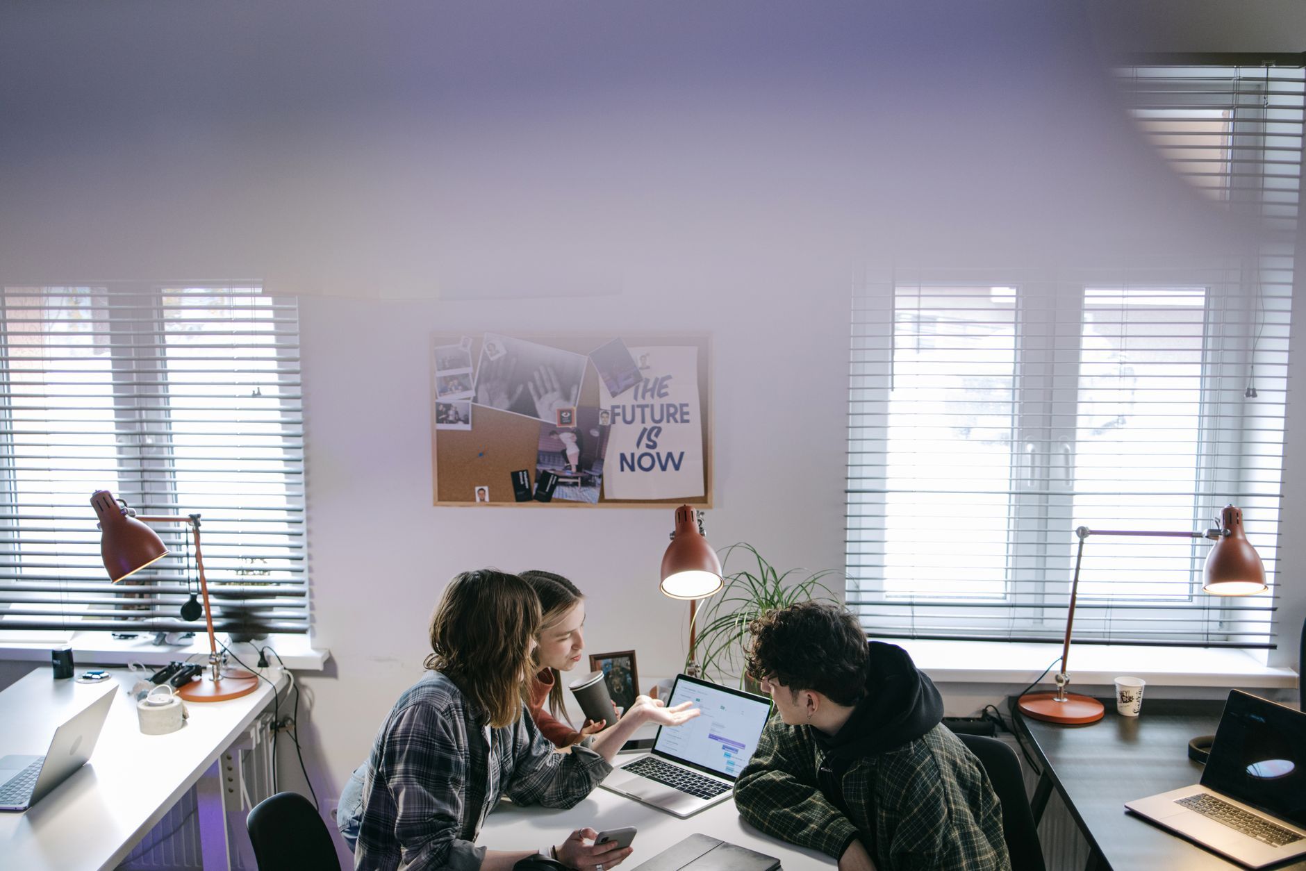 A small team gathered around laptops in a bright office, discussing findings together, representing a Hong Kong nonprofit reviewing the results of a free Microsoft 365 security check