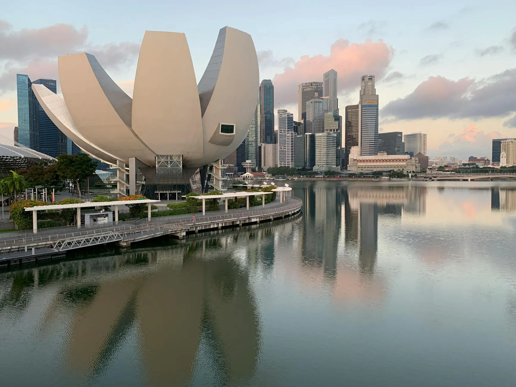 ArtScience Museum reflecting in Marina Bay with Singapore skyline at sunrise.