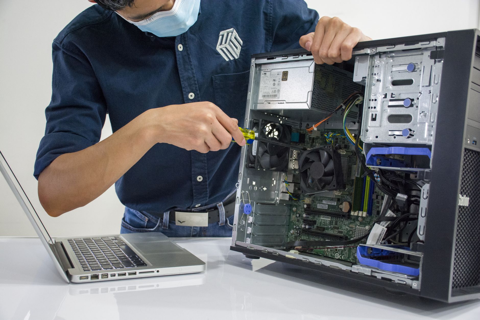 A technician working hands-on at a desktop computer in an office — the physical layer of IT support that no remote service desk can absorb, and the reason a Hong Kong office has to choose between an embedded engineer, scheduled half-days and per-visit dispatch