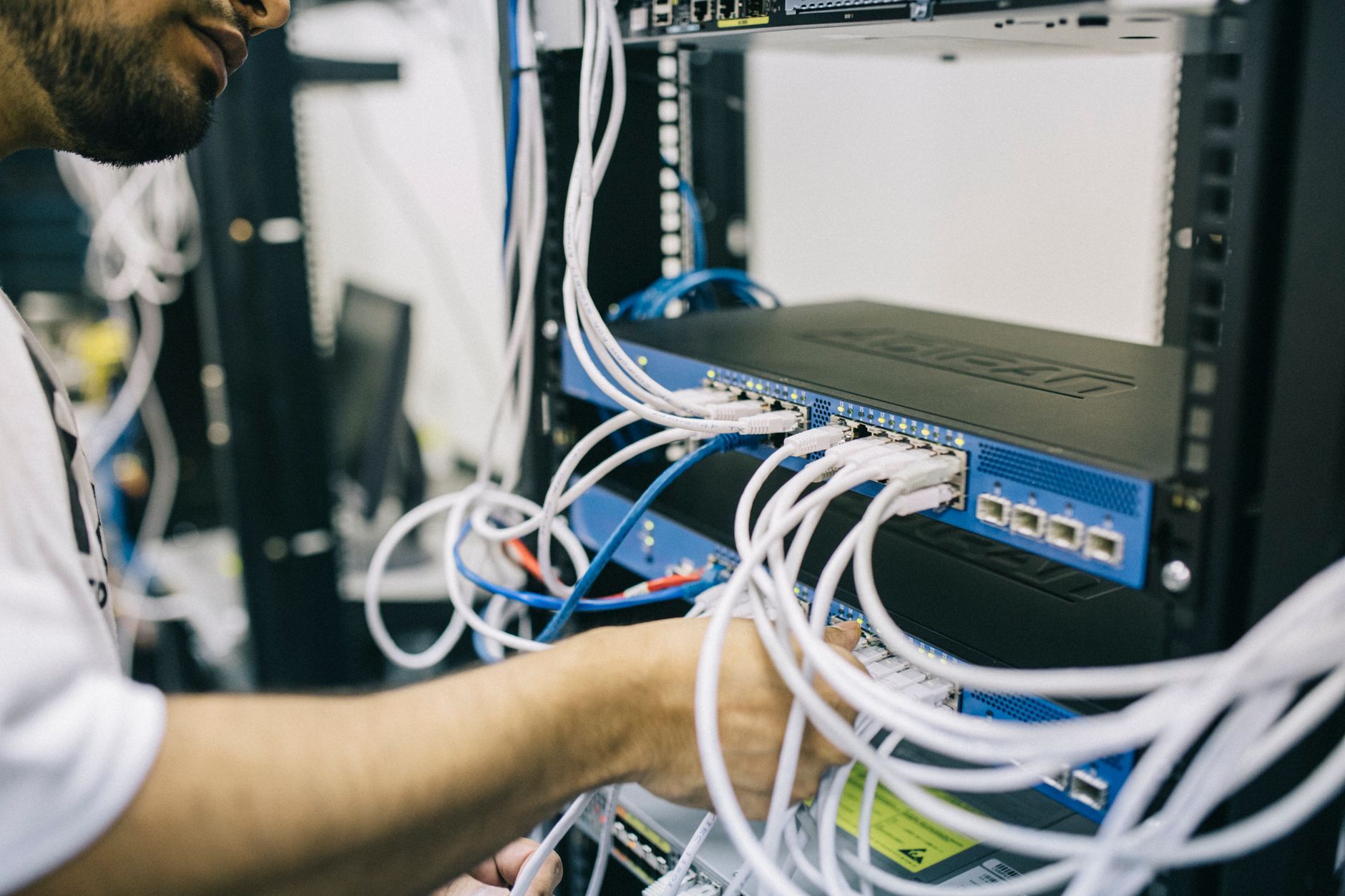 An engineer working on network cabling in a rack, standing for the controller somebody has to keep running long after the access points are on the wall