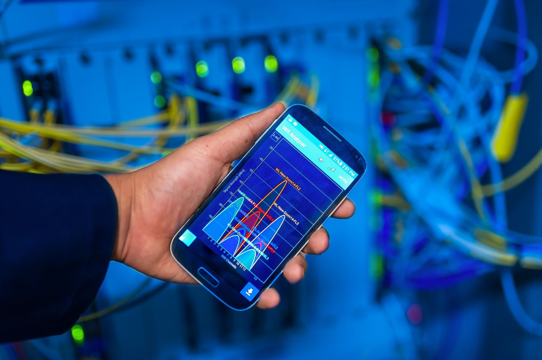 A hand holding a phone showing network analysis data in a network equipment room