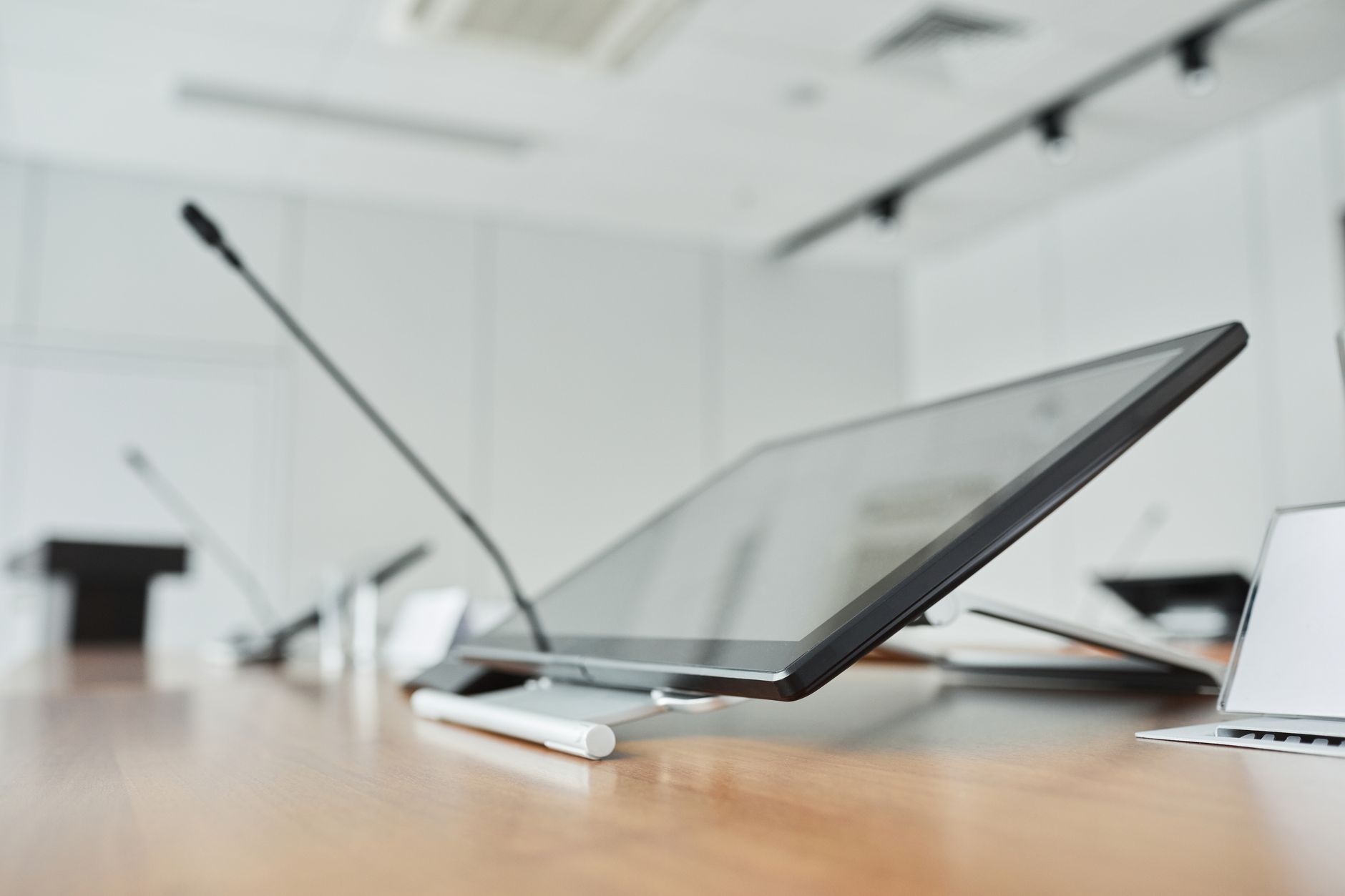 Empty modern conference room with a wall-mounted digital screen and table microphones on a wooden table, the kind of room that needs AV support.