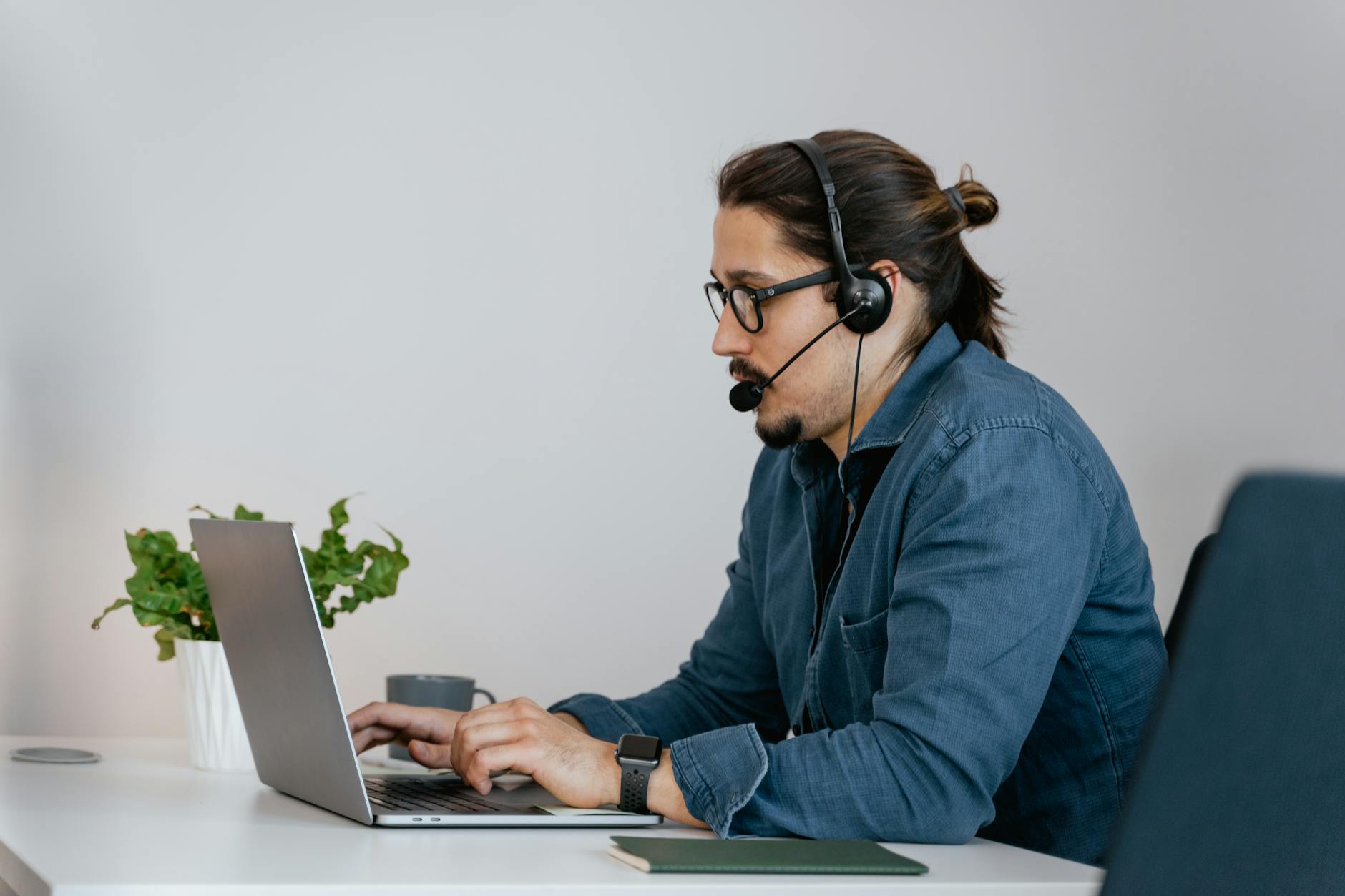 Adult man wearing a headset working on a laptop in an office space.