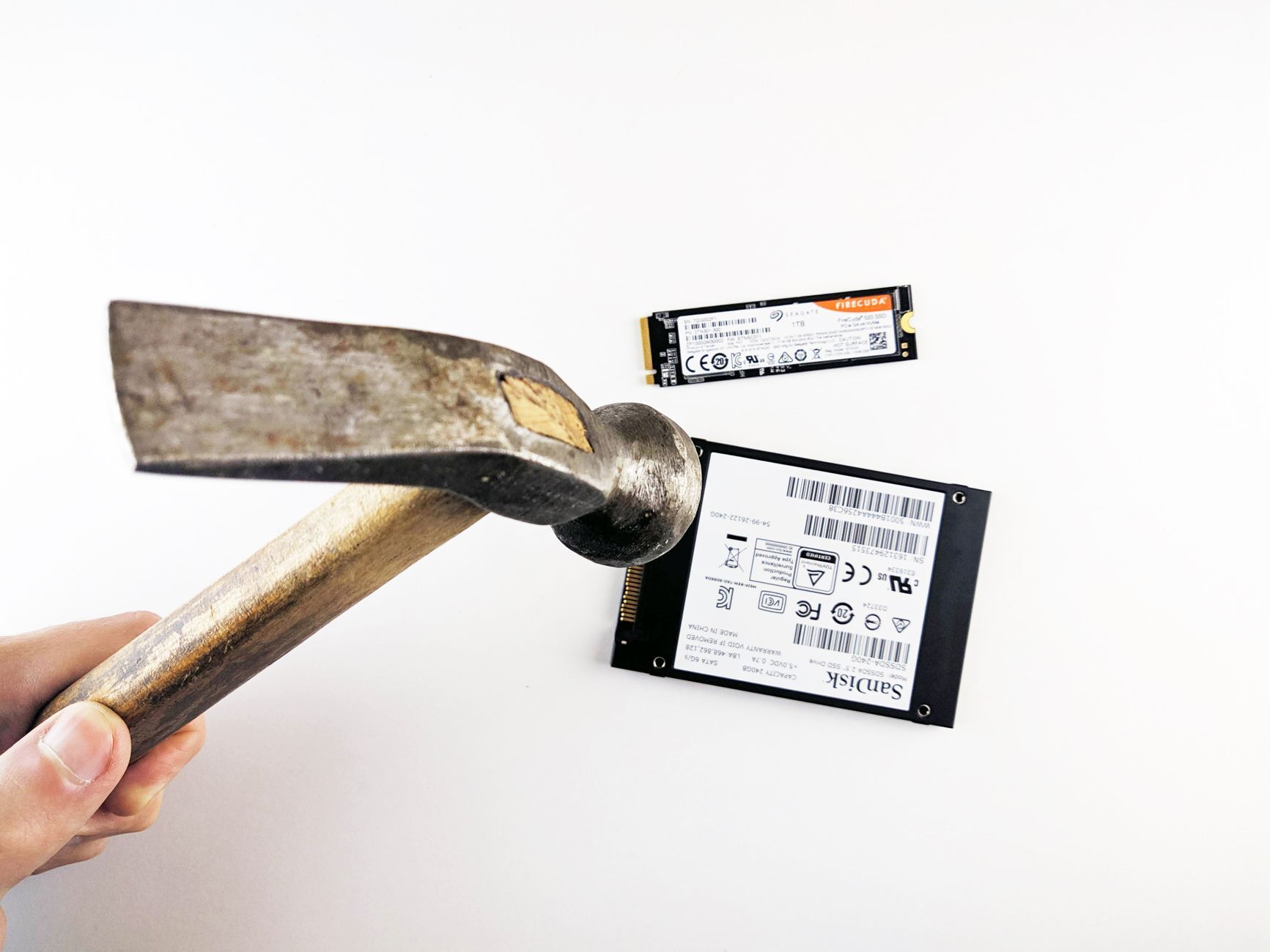 A hammer poised to strike a hard drive and SSD on a workbench — the physical destruction step behind a data-erasure certificate, and the kind of evidence a multi-country IT asset disposal programme has to document per device