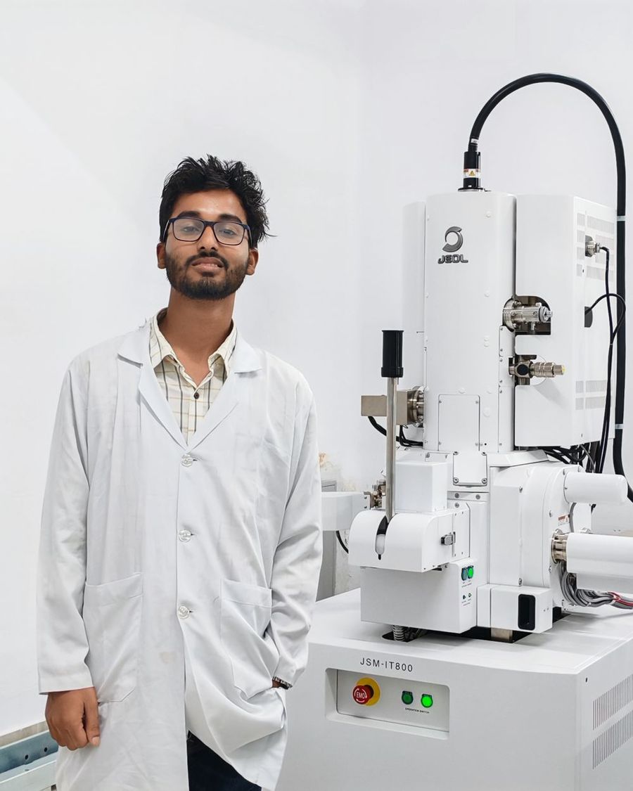 Shohag in a lab coat beside a scanning electron microscope