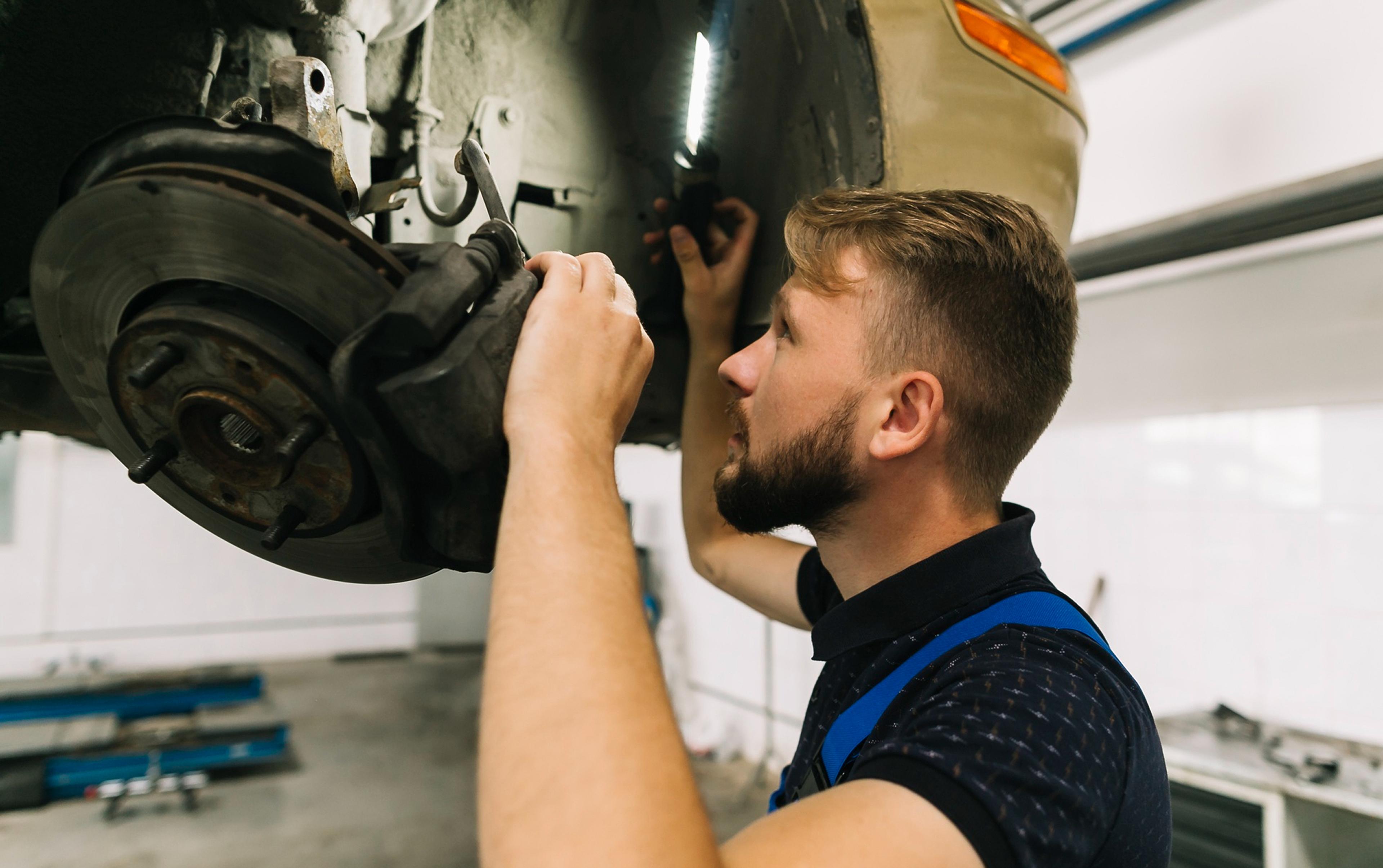 Mechanic inspects the brake system on a raised vehicle using a work light.