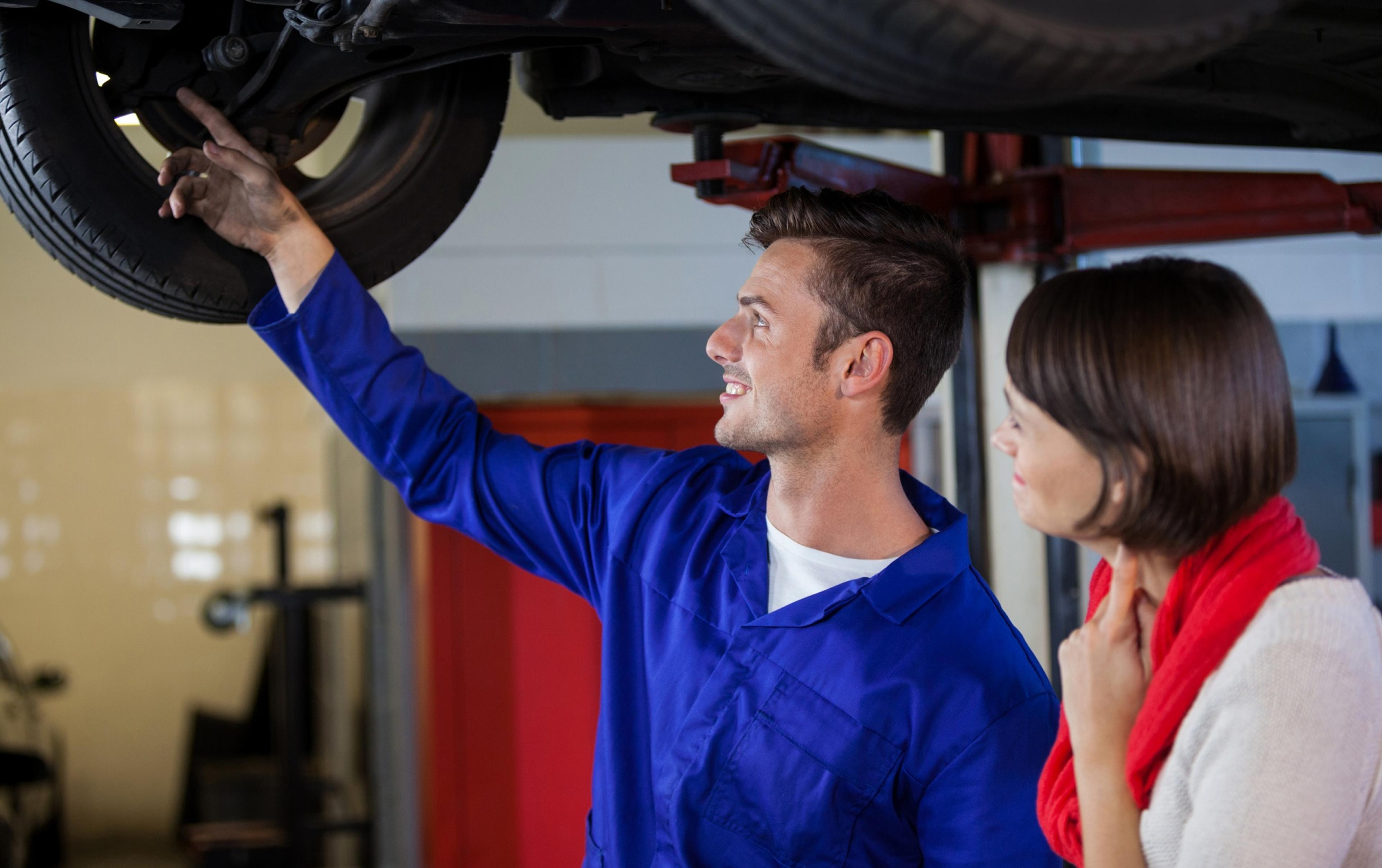 Mechanic explaining the condition of a tire to a customer under a lifted car in a workshop