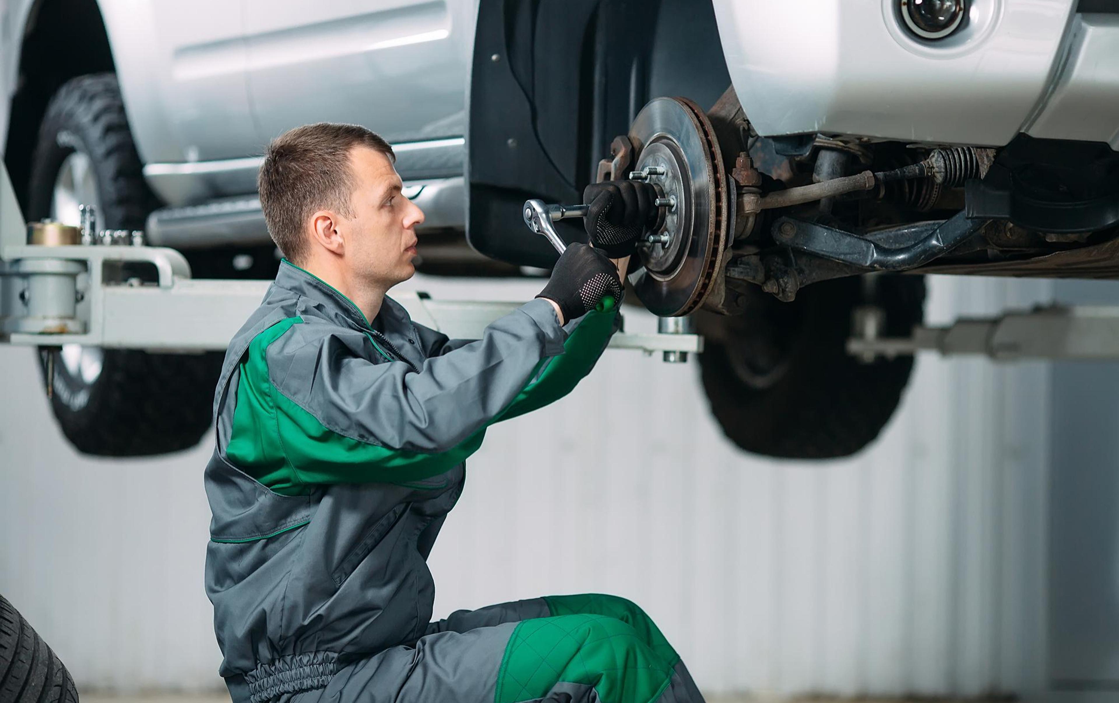 Mechanic installing a brake disc on the front axle of a raised vehicle in the workshop