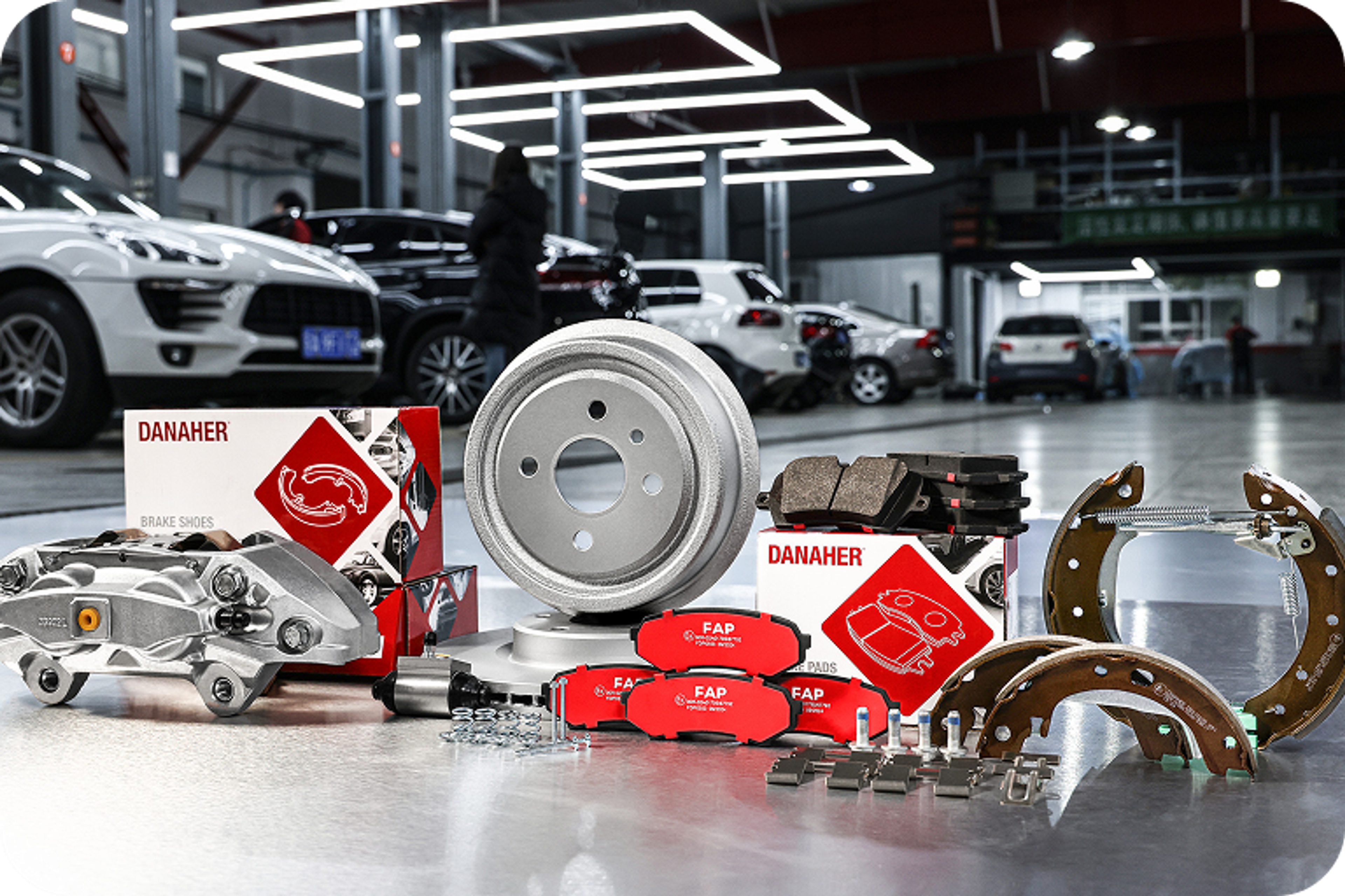 Danaher brake components such as brake discs, brake calipers, brake pads, and drum brake parts, presented in a modern automotive workshop.