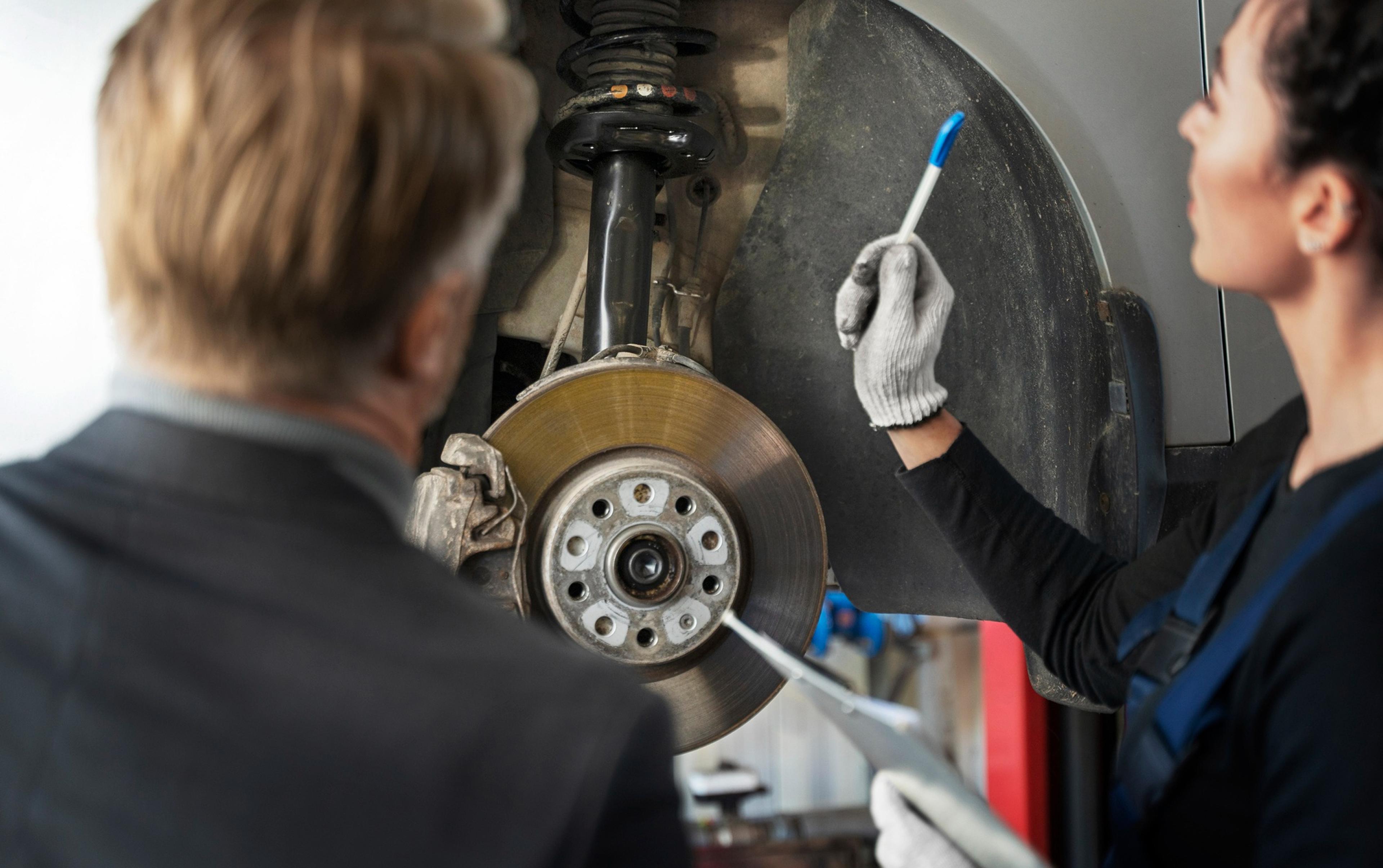 A mechanic explains the brake system of a car to a customer in the workshop.