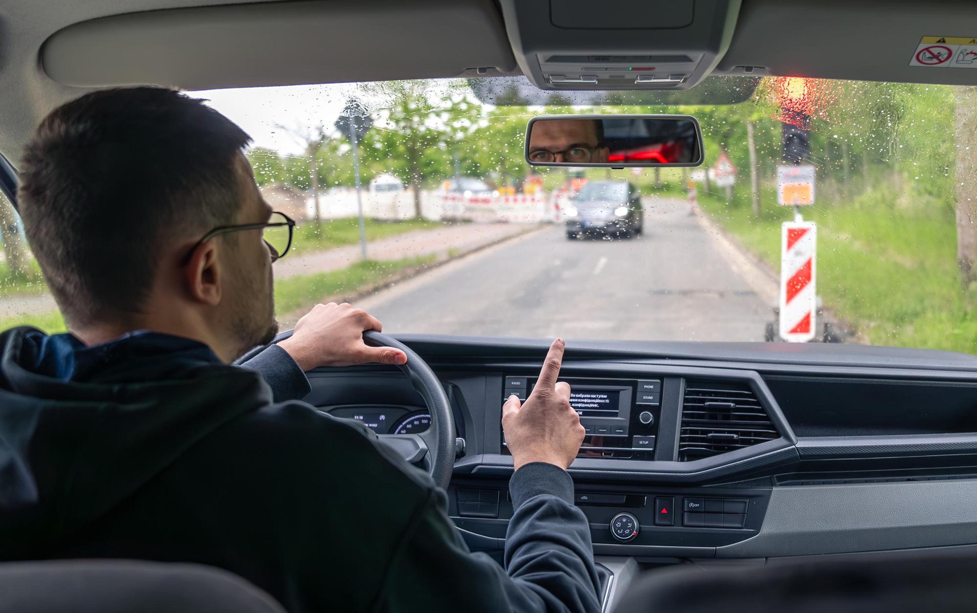 Autofahrer steht bei Regen an einer roten Ampel und hebt den Finger als Gestik.