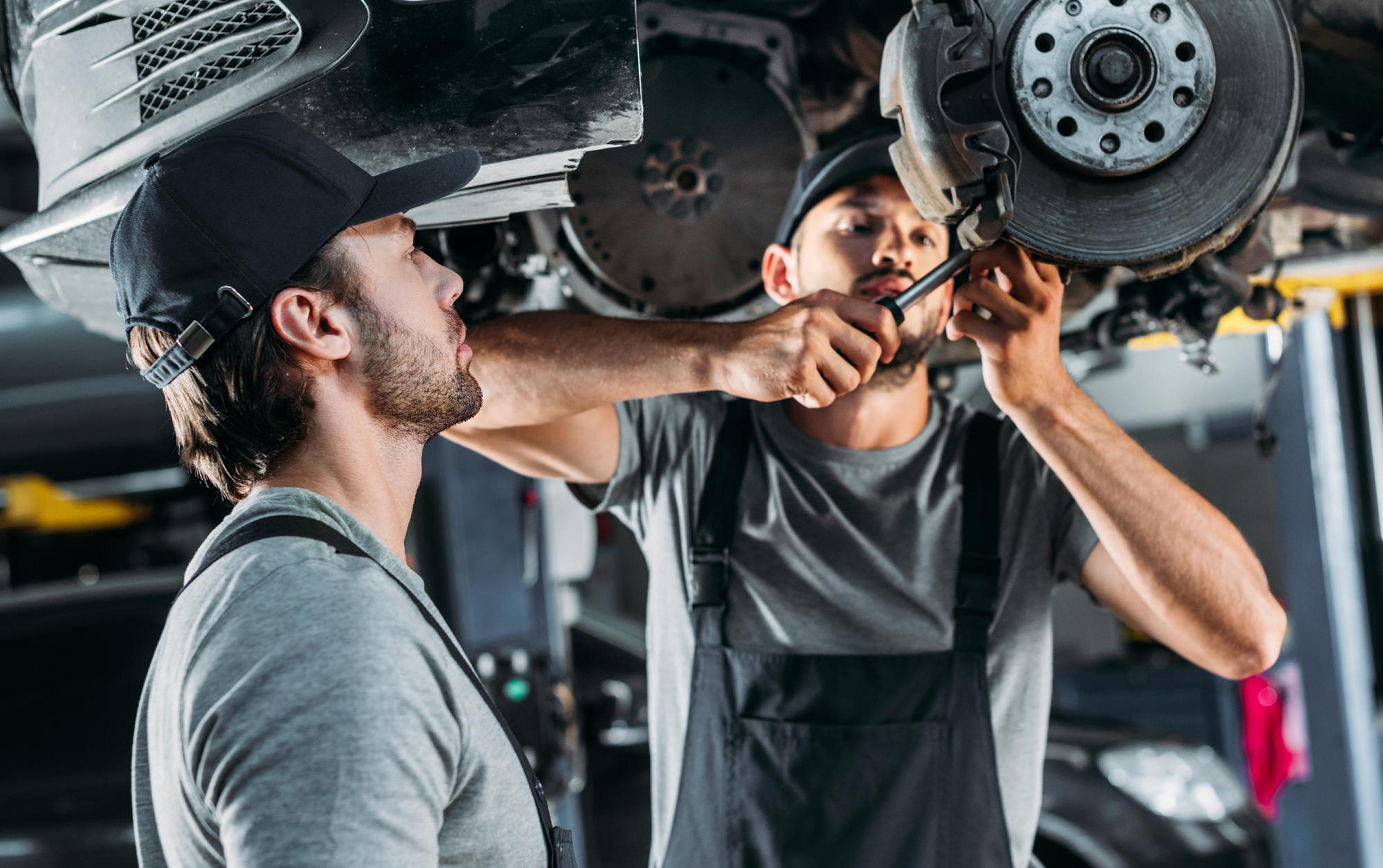 Two car mechanics are working under a raised vehicle, installing a brake system in the car repair shop.