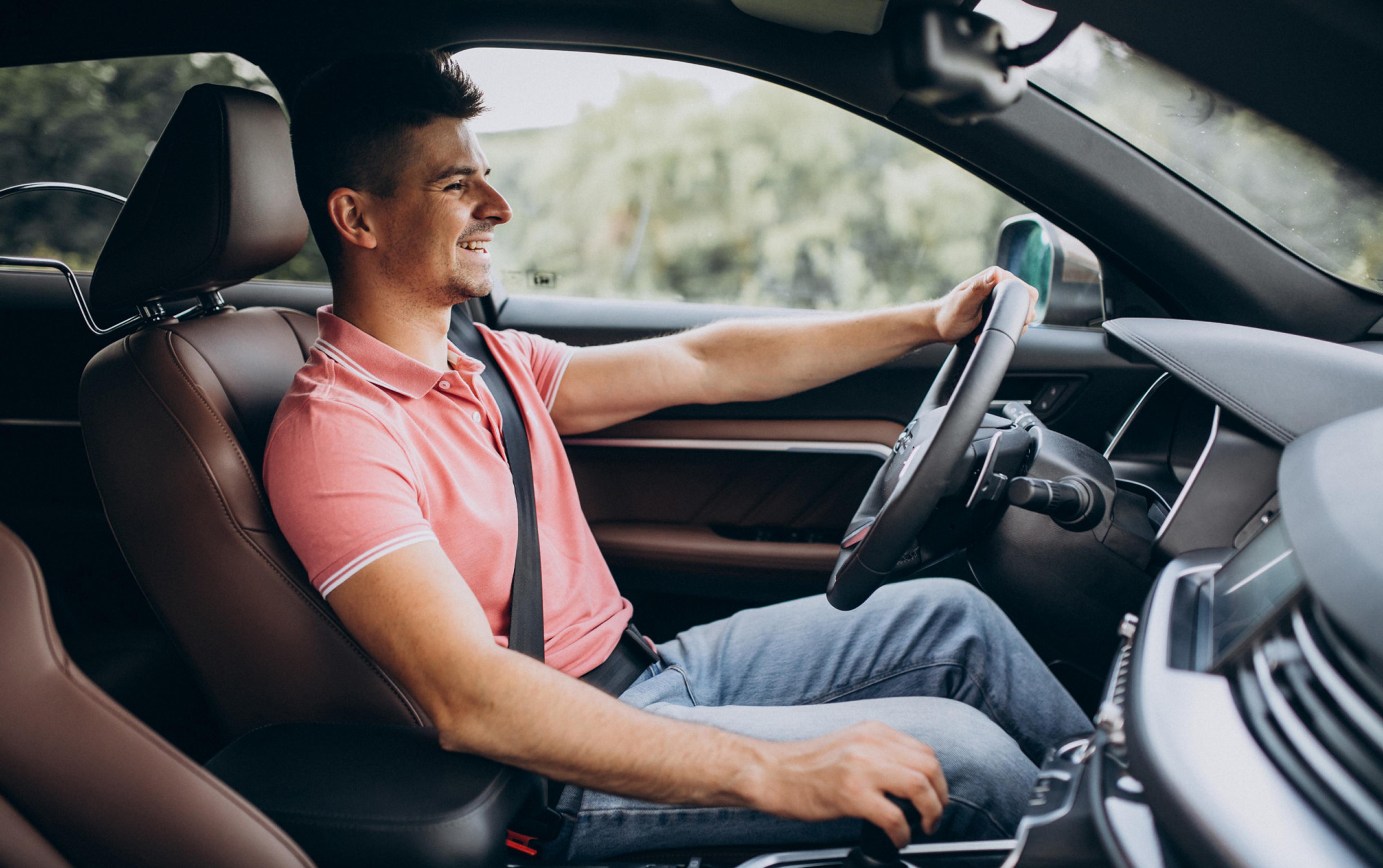 A man sits behind the wheel of a modern car, wearing a seatbelt, and drives relaxed along a country road.