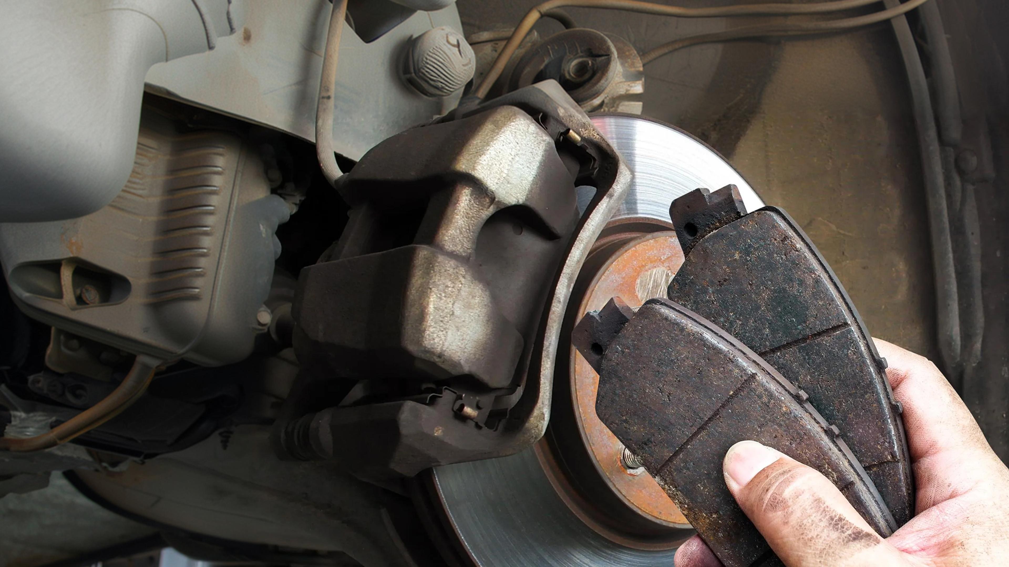 Worn brake pads in front of a brake disc in the removed state on the vehicle