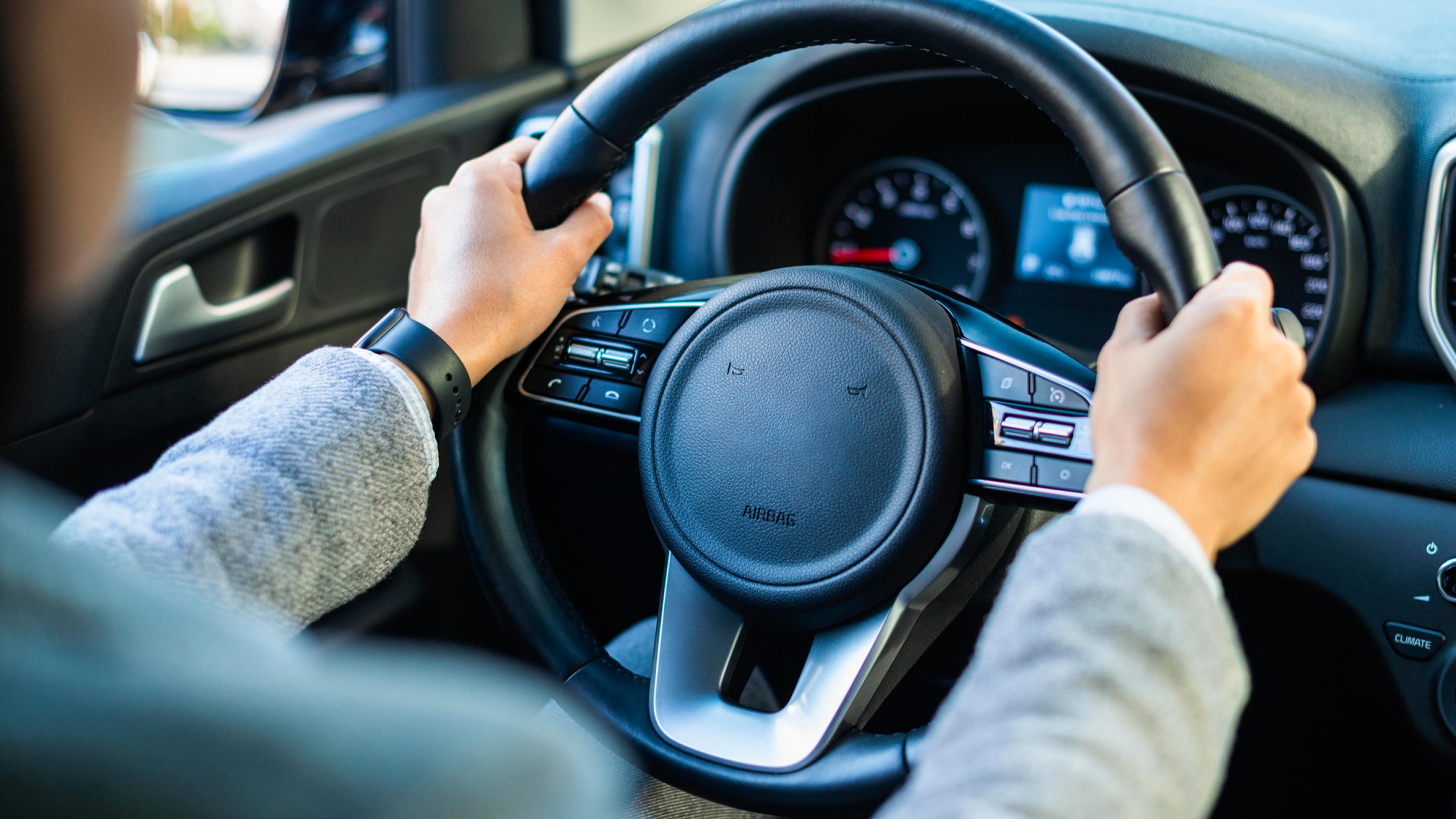 Close-up of hands on the steering wheel of a modern car with a view of the dashboard.
