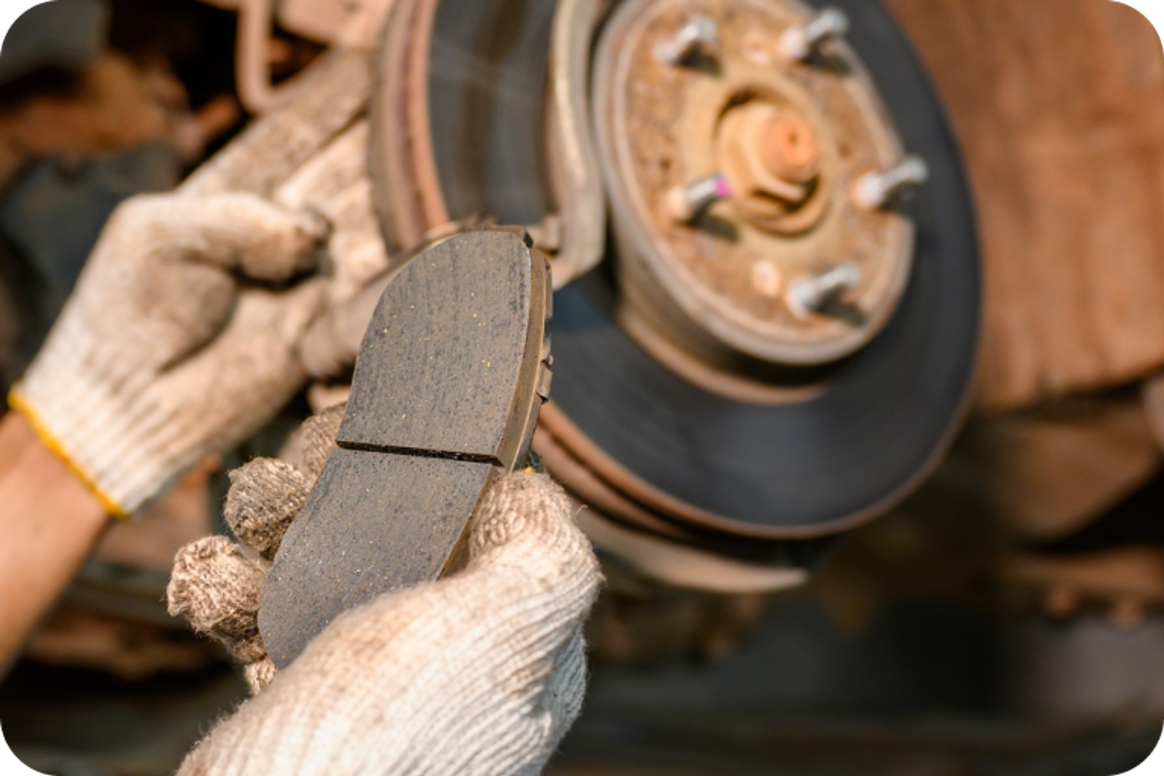 Mechanic holding a worn brake pad in front of a brake disc mounted on a vehicle wheel