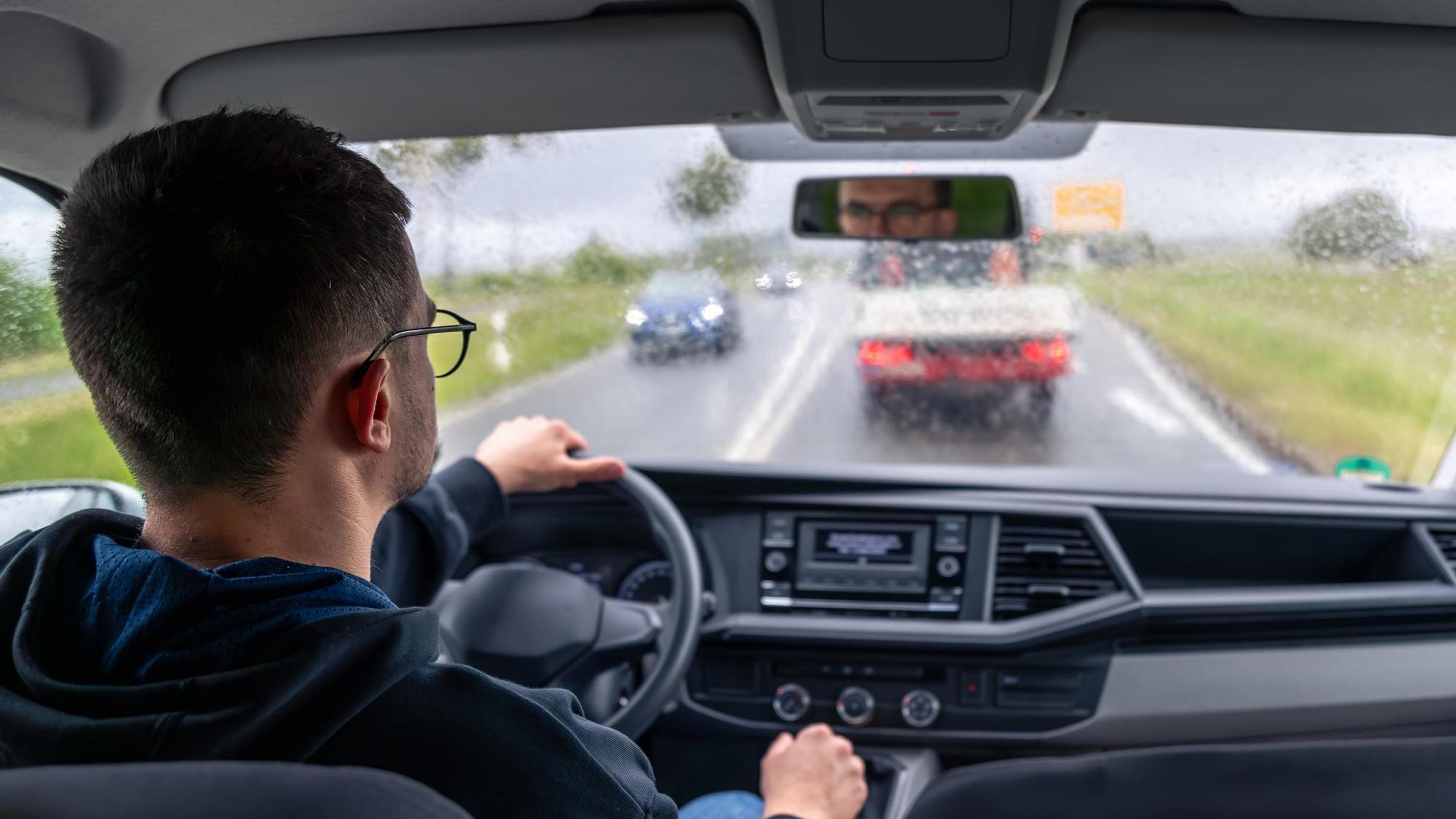 View from behind of a driver driving on a country road in the rain with oncoming traffic.