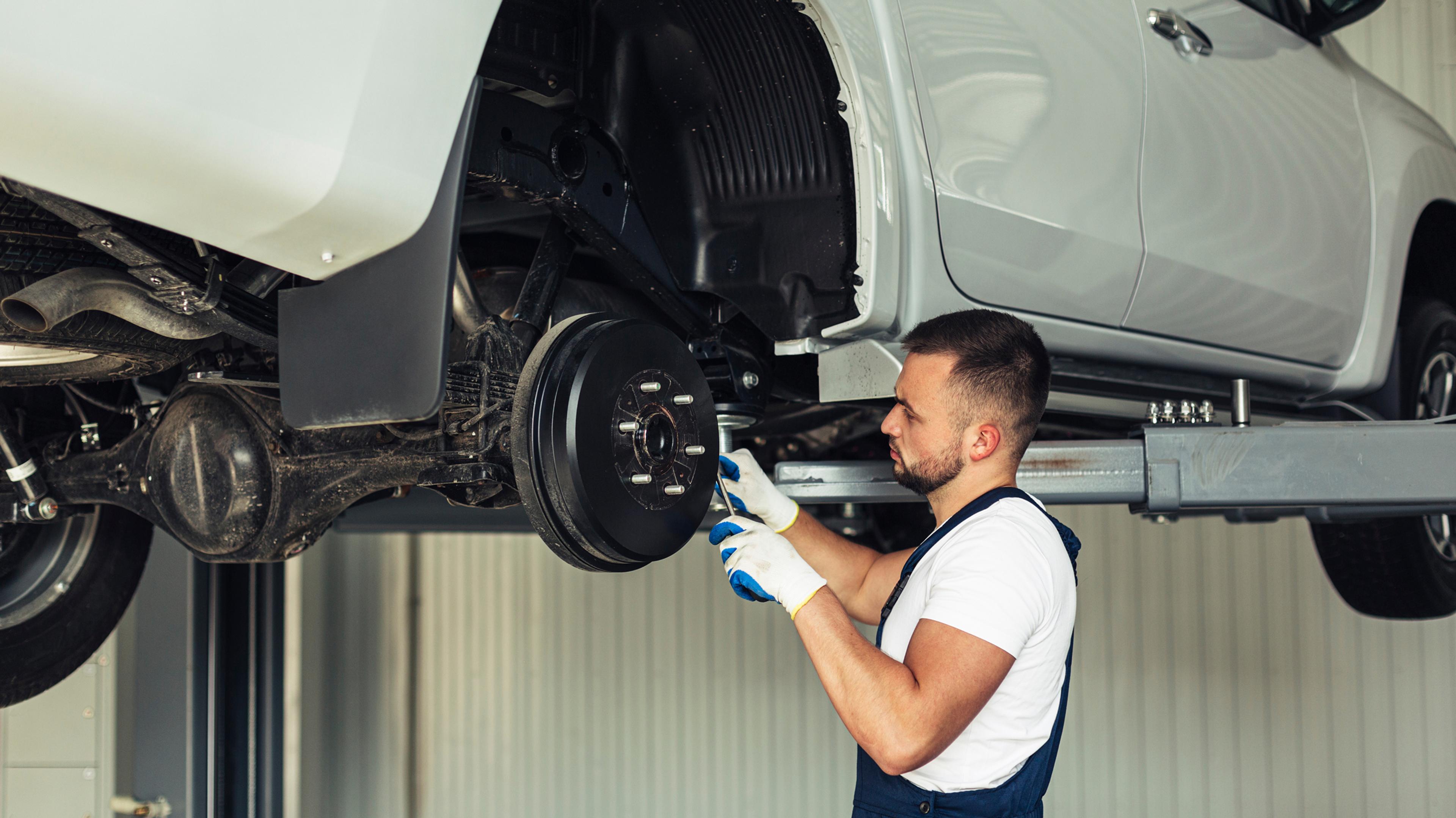 Mechanic inspecting a drum brake on a lifted car in a workshop