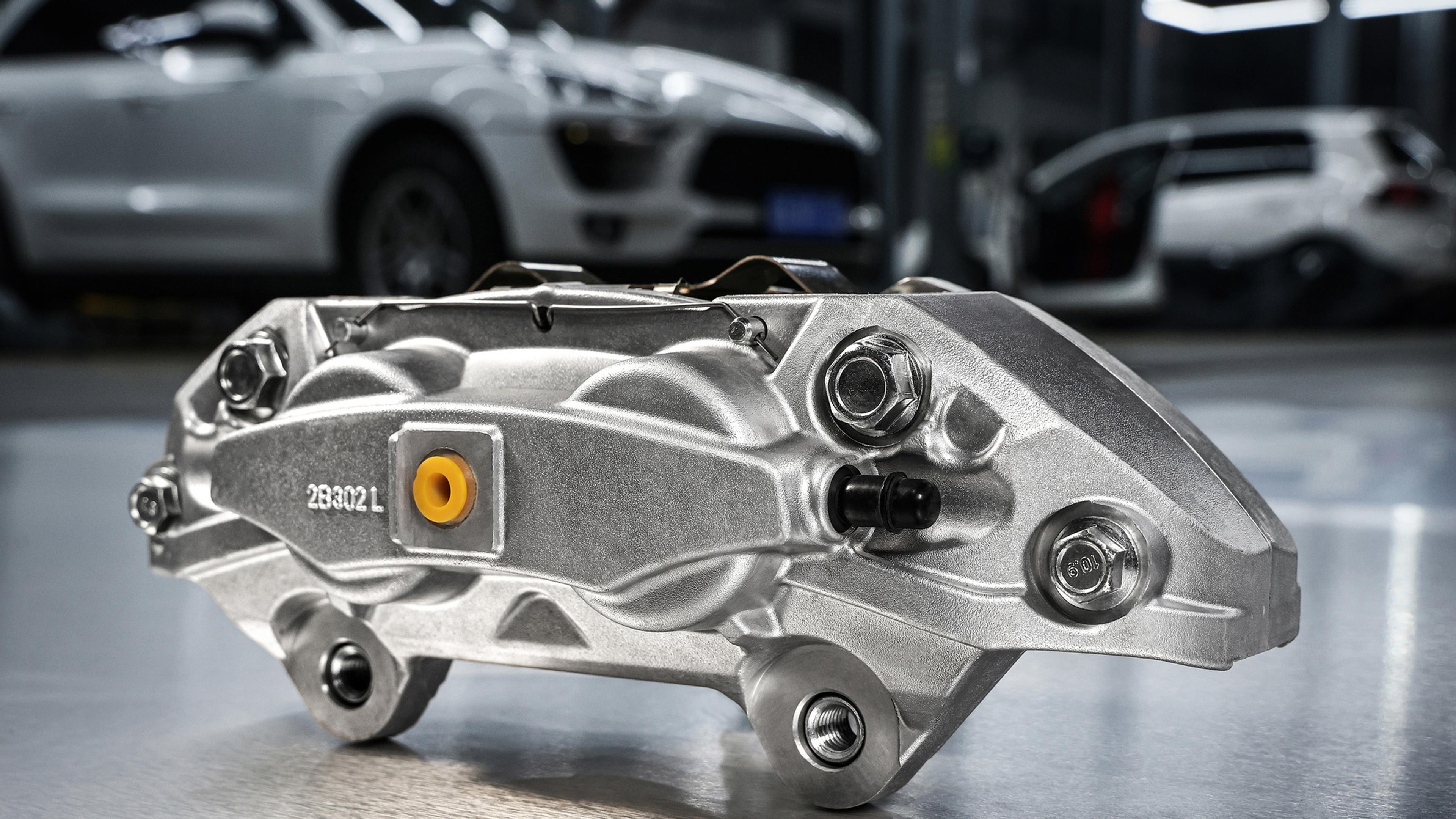 Bremssattel als einzelnes Bauteil auf Werkstattboden mit Autos im Hintergrund