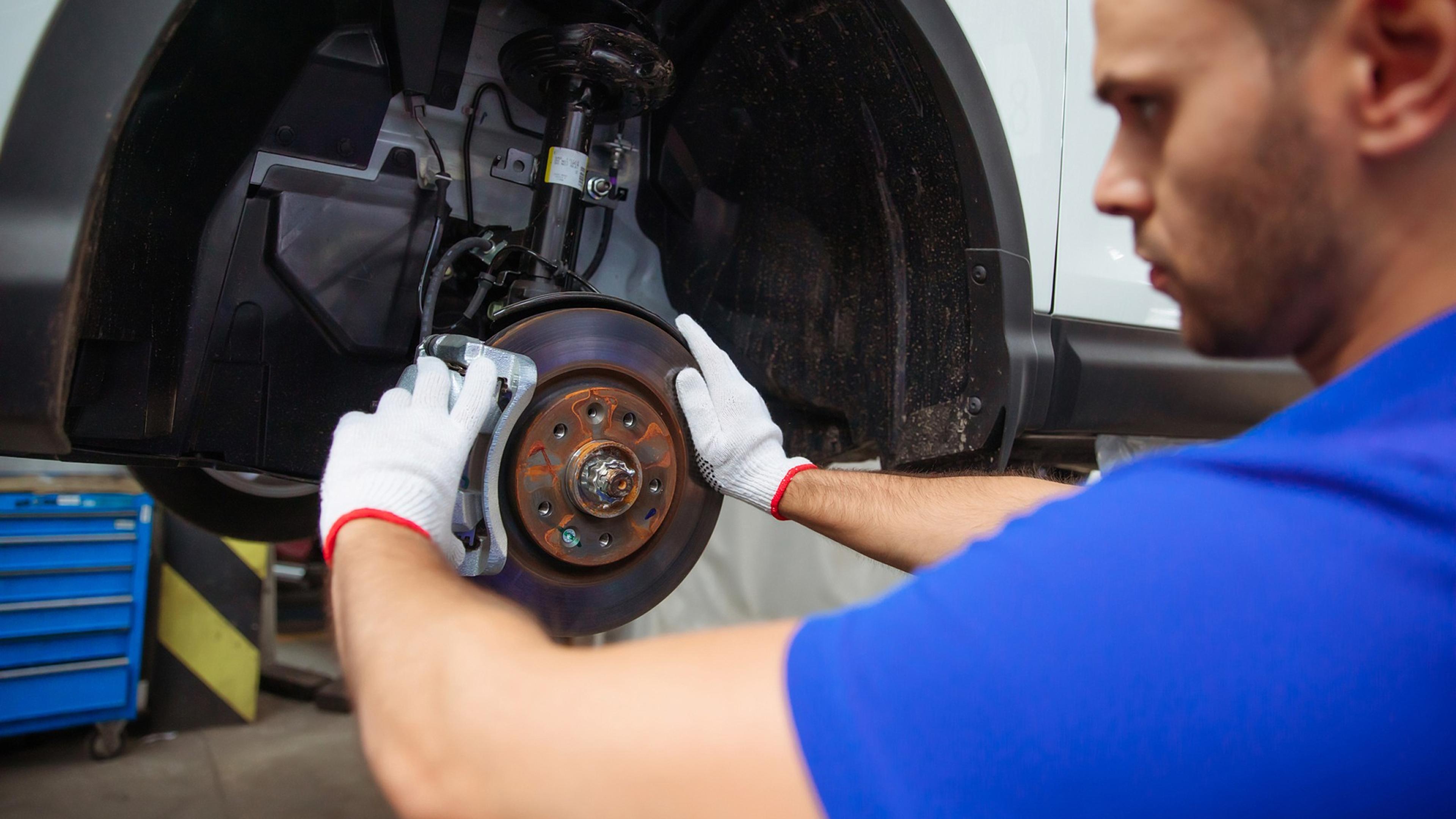 Mechanic installing a brake caliper on a lifted car in a workshop