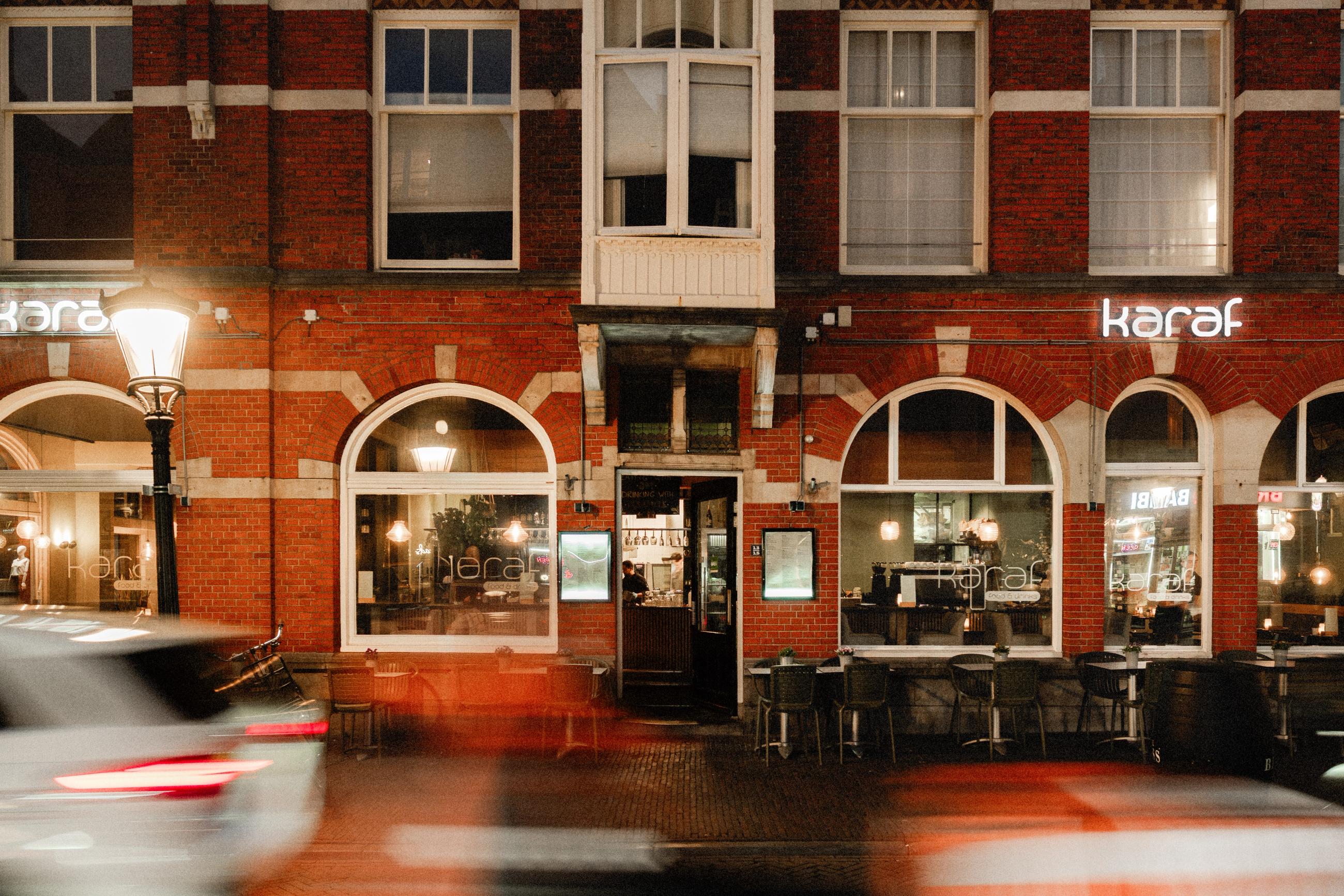 Restaurant Karaf aan de Lange Nieuwstraat in Utrecht 's avonds, met verlichte gevel en voorbijrijdende auto's