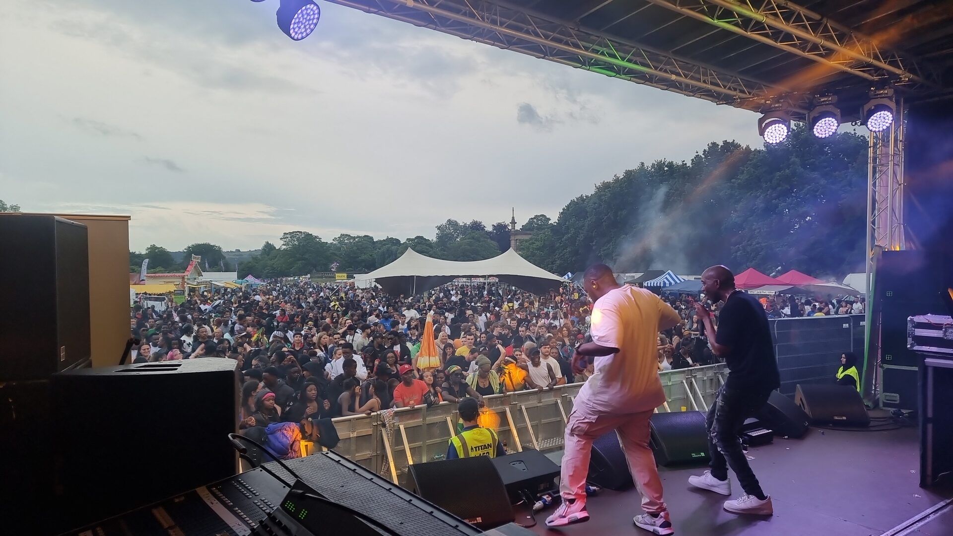 Performers on the carnival main stage with a packed crowd in Greenhead Park at dusk.
